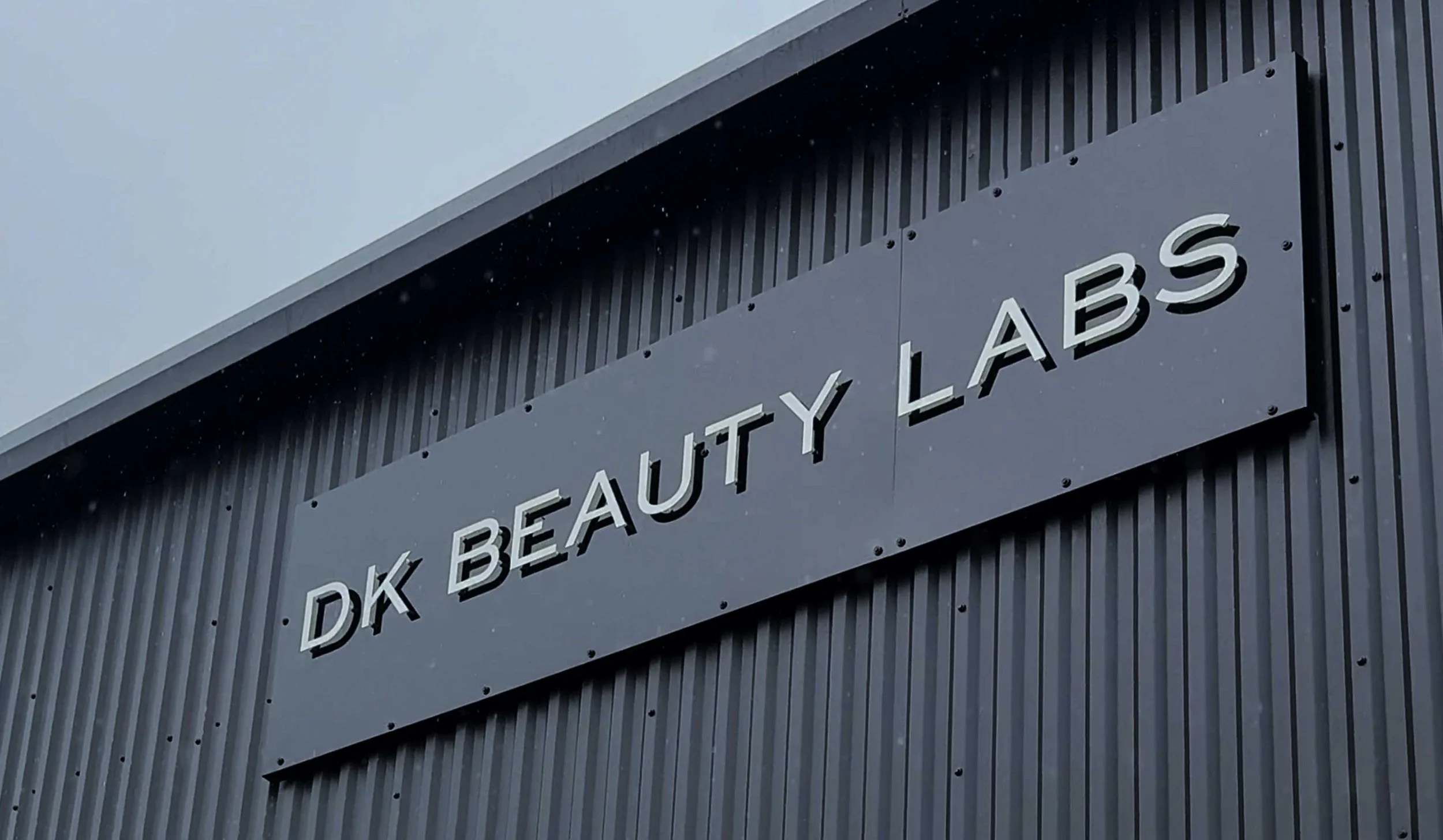 Exterior view of a building with a sign reading "DK BEAUTY LABS" on a dark corrugated wall.