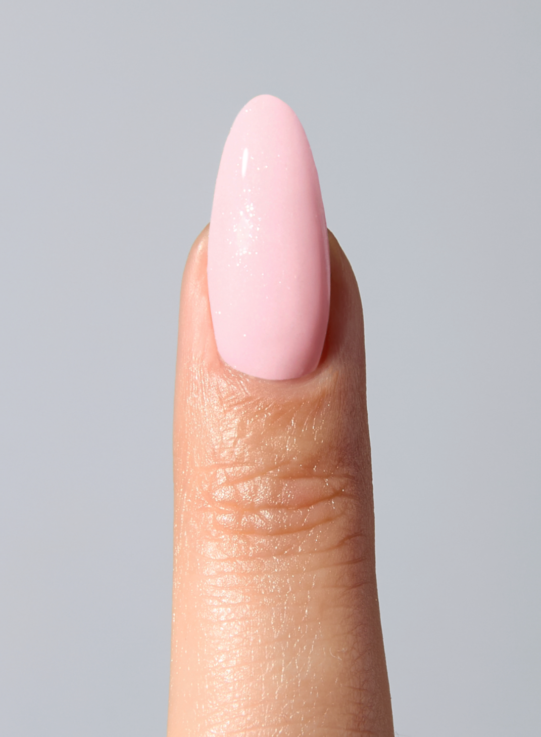 Close-up of a finger with a painted pink almond-shaped nail against a light grey background.