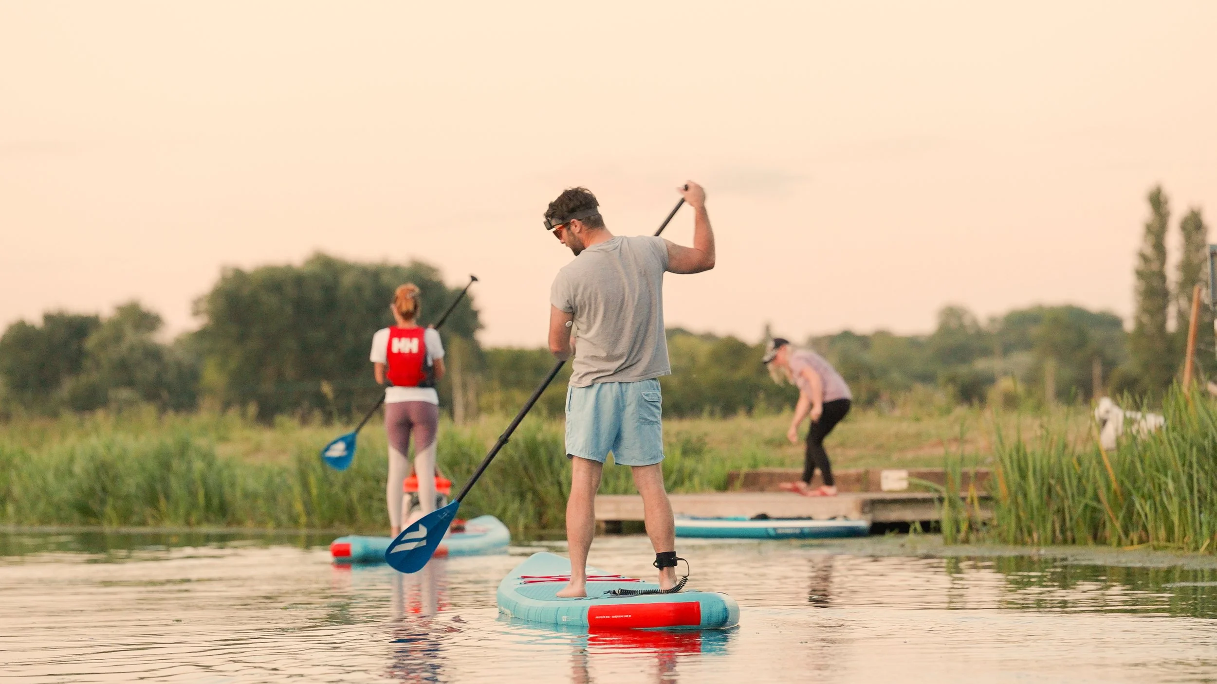 People paddleboarding and preparing to get off the water at sunset on a calm river surrounded by greenery.