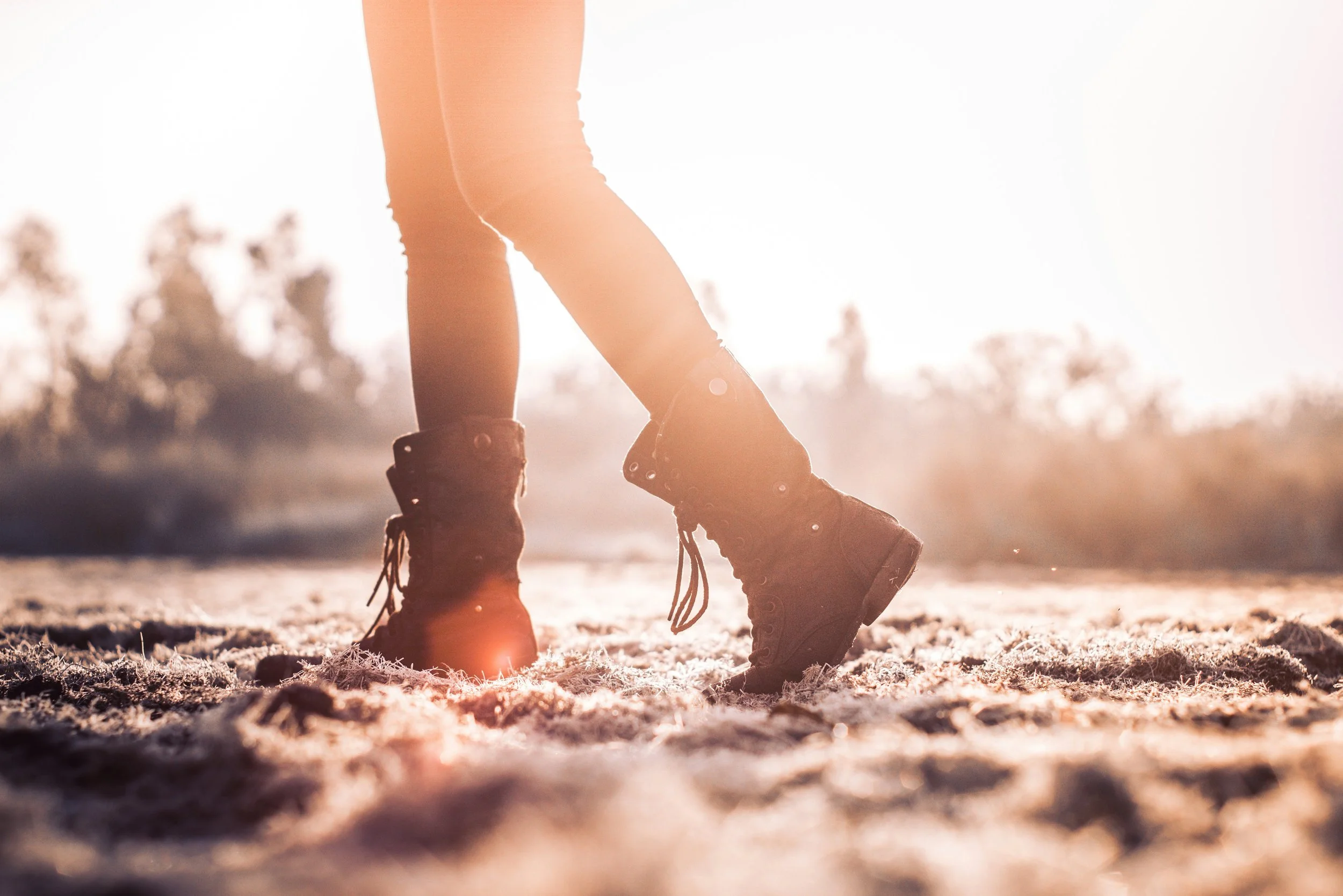 Person wearing combat boots jumping in a sandy outdoor area during sunset.