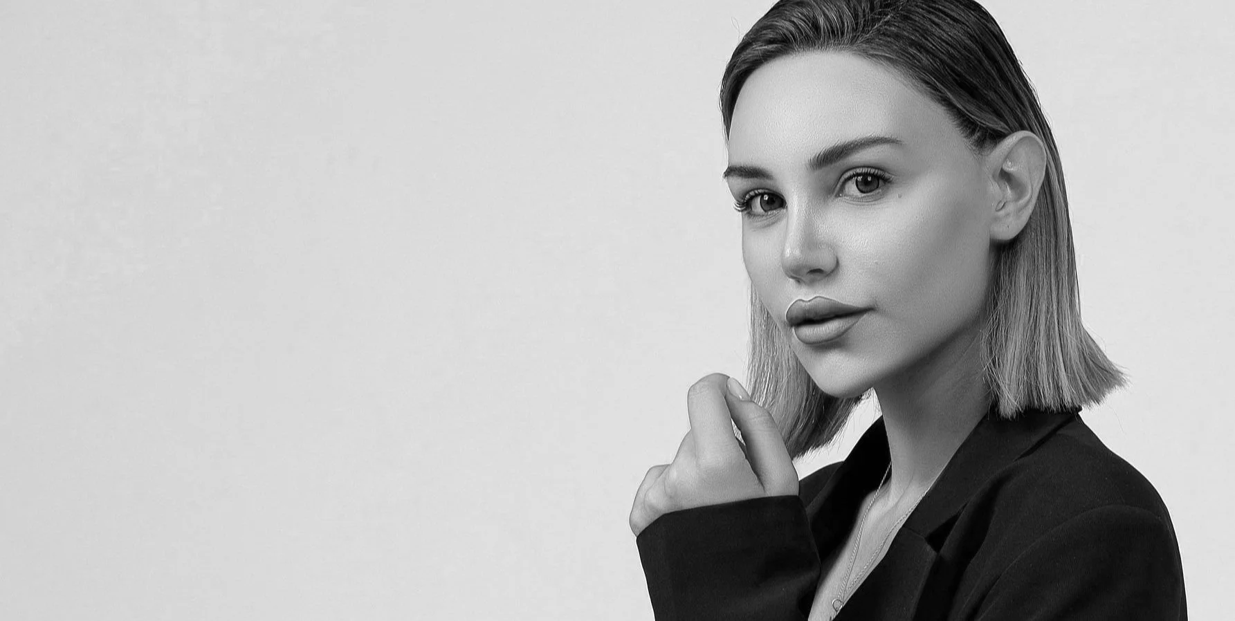Black and white portrait of a woman with shoulder-length hair, wearing a blazer, looking at the camera with a subtle smile, against a plain background.