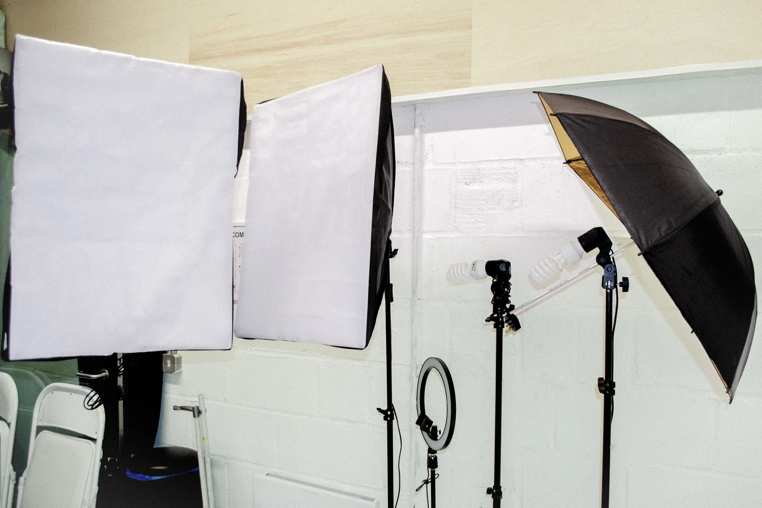 Photography lighting equipment including softboxes, umbrellas, and lights mounted on stands in a photography studio or setup.