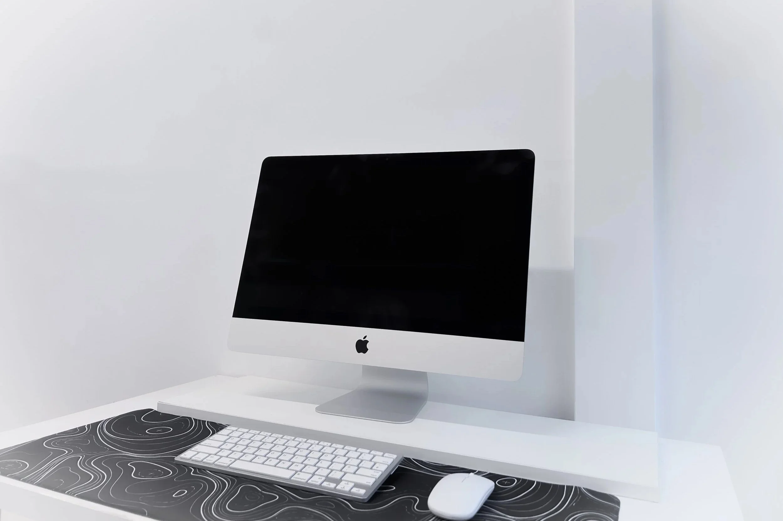 Apple iMac computer with keyboard and mouse on a white desk with black and white patterned mouse pad
