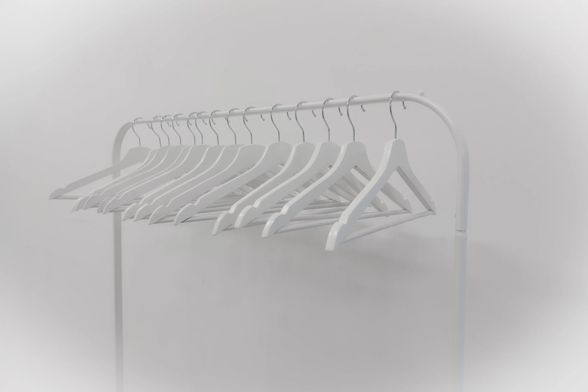 A row of empty white coat hangers hanging on a white metal clothing rack against a plain white background.