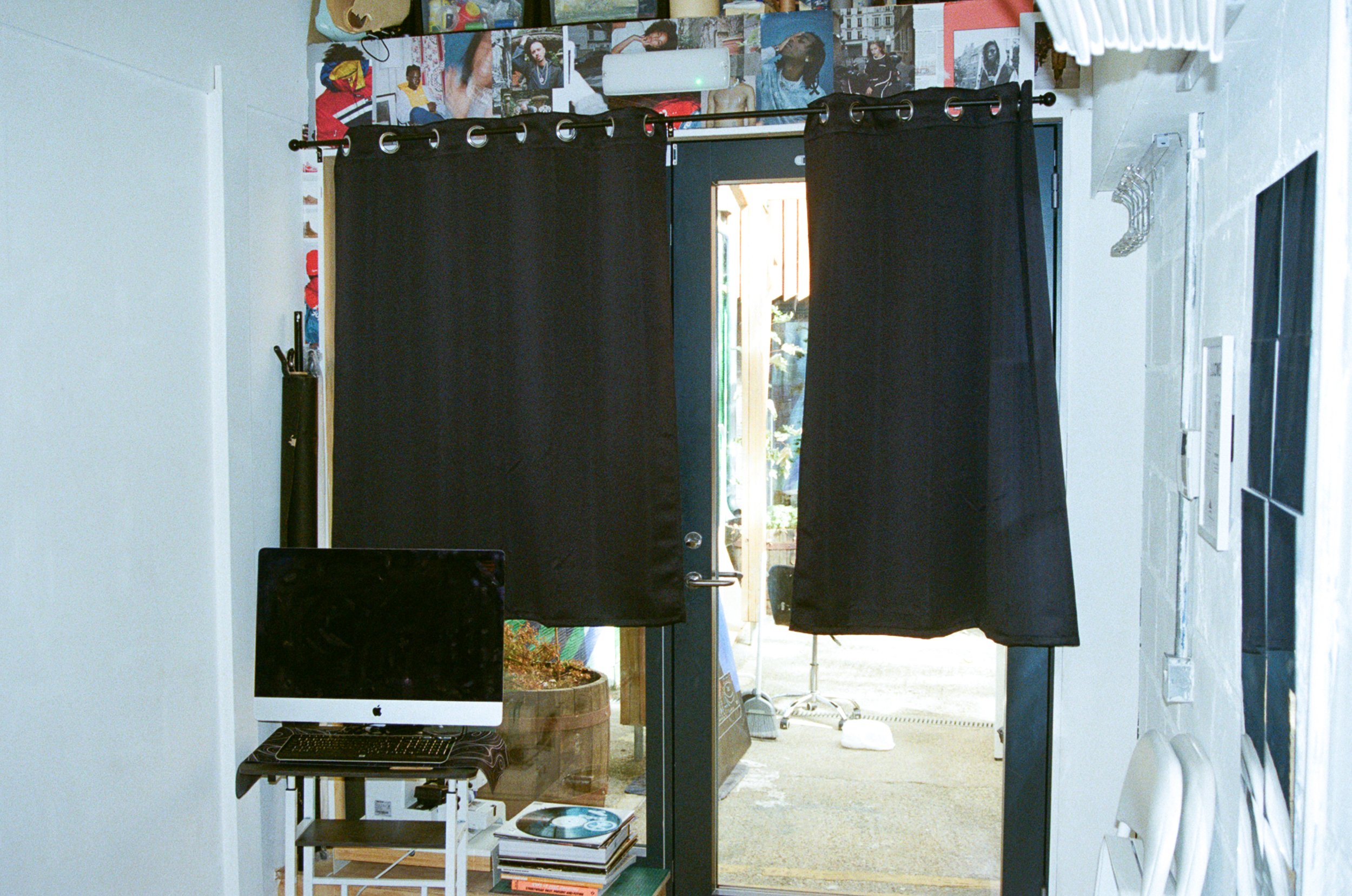 A doorway with black curtains in a room decorated with posters and photographs, leading to an outdoor space.
