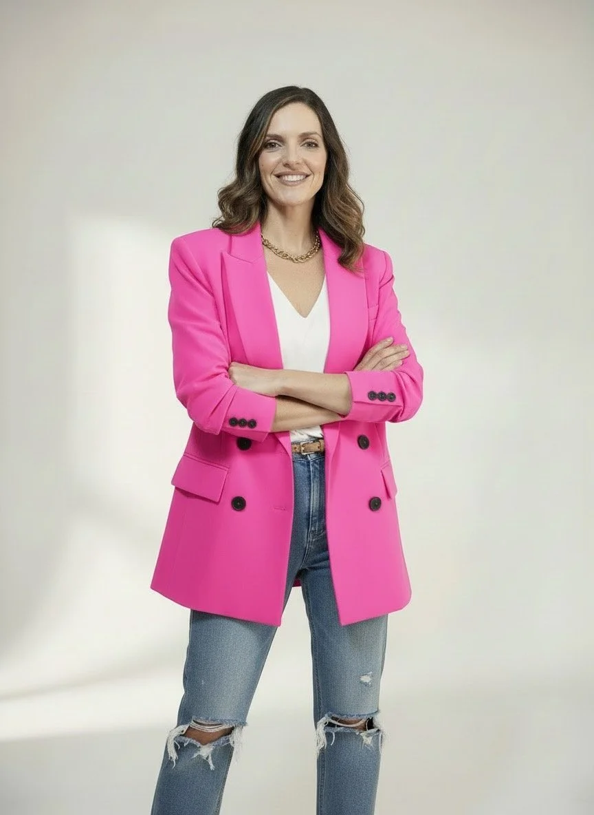 Livi smiling with her arms crossed. She's wearing a bright pink jacket and ripped jeans.