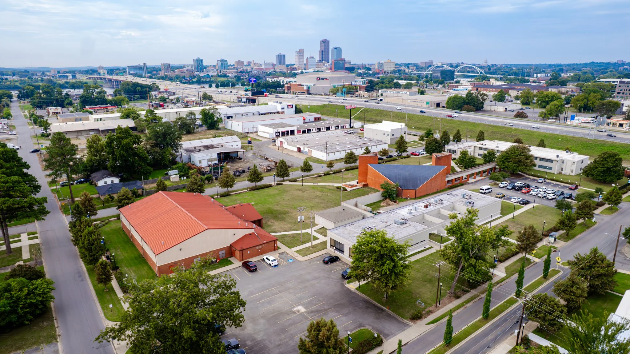 Aerial view of a cityscape with buildings, trees, roads, and parking lots, featuring a mix of commercial and residential areas.