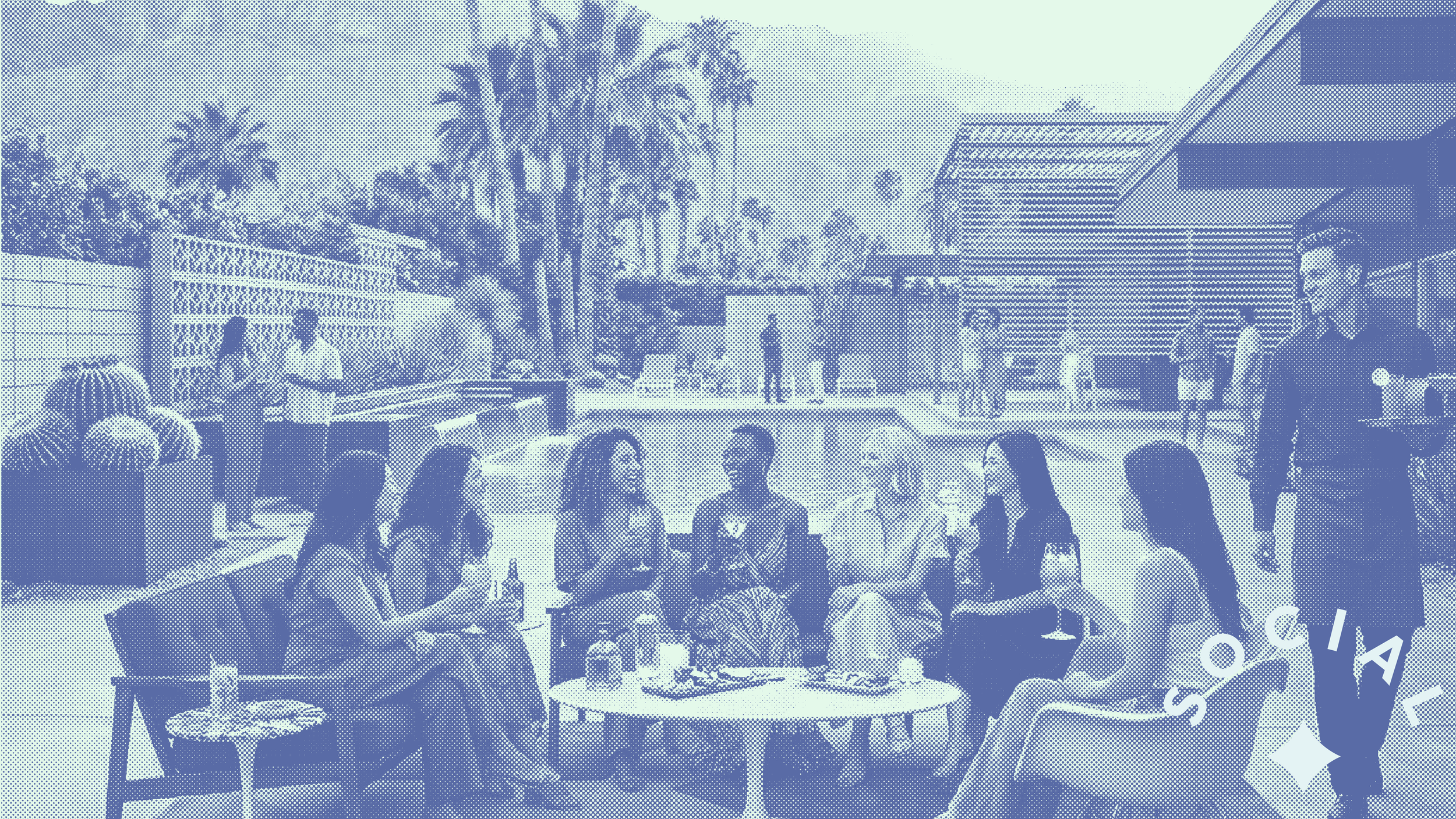 Group of young women sitting and talking around a table outdoors at a social gathering, with palm trees and modern buildings in the background.