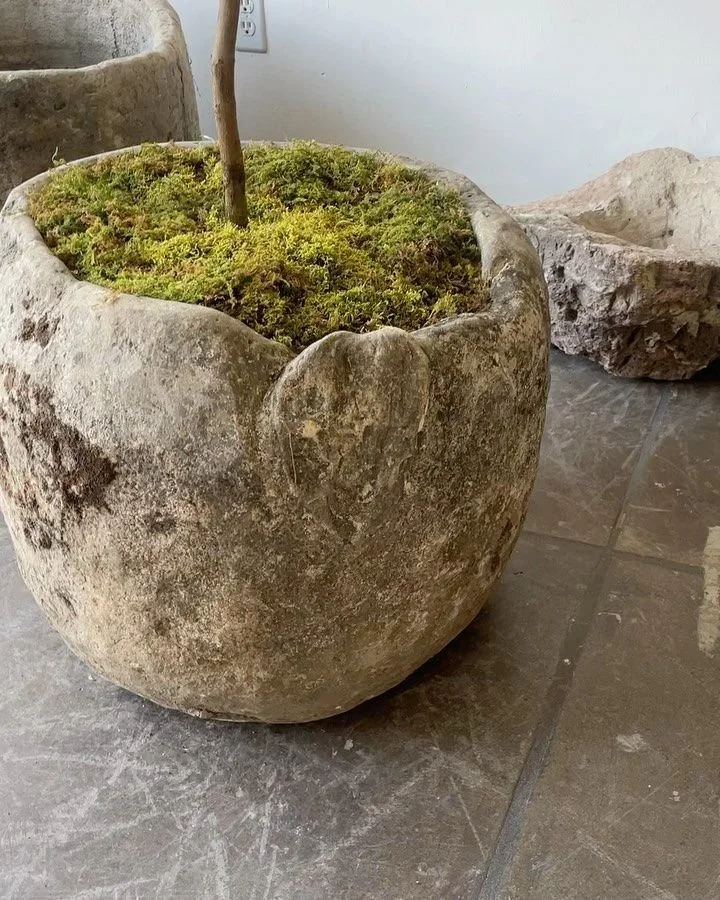 Cream-colored woven rug with diamond and floral pattern and fringed edges hanging outdoors against a wooden structure.