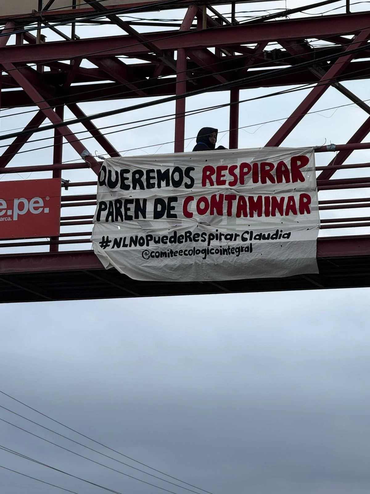 Pancarta colgada en un puente que dice: "Queremos respirar. Paremos de contaminar. #NLNOpuedeRespirar Claudia @comiteecologicointegral" y una persona observando desde arriba.