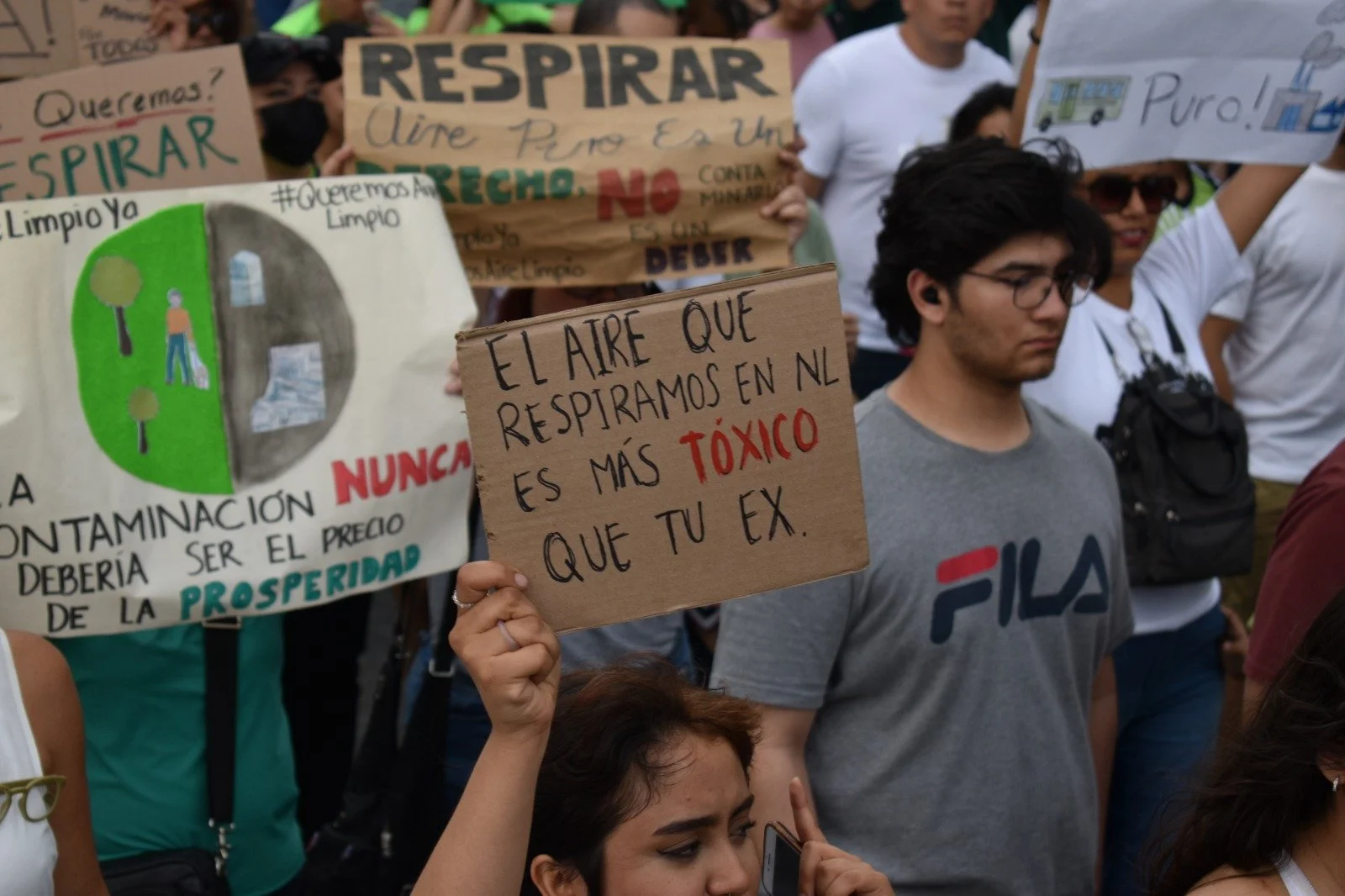 Un grupo de personas en una protesta sosteniendo carteles con mensajes sobre el medio ambiente y el aire. Uno de los carteles dice: 'El aire que respiramos en NL es más tóxico que tu ex'.