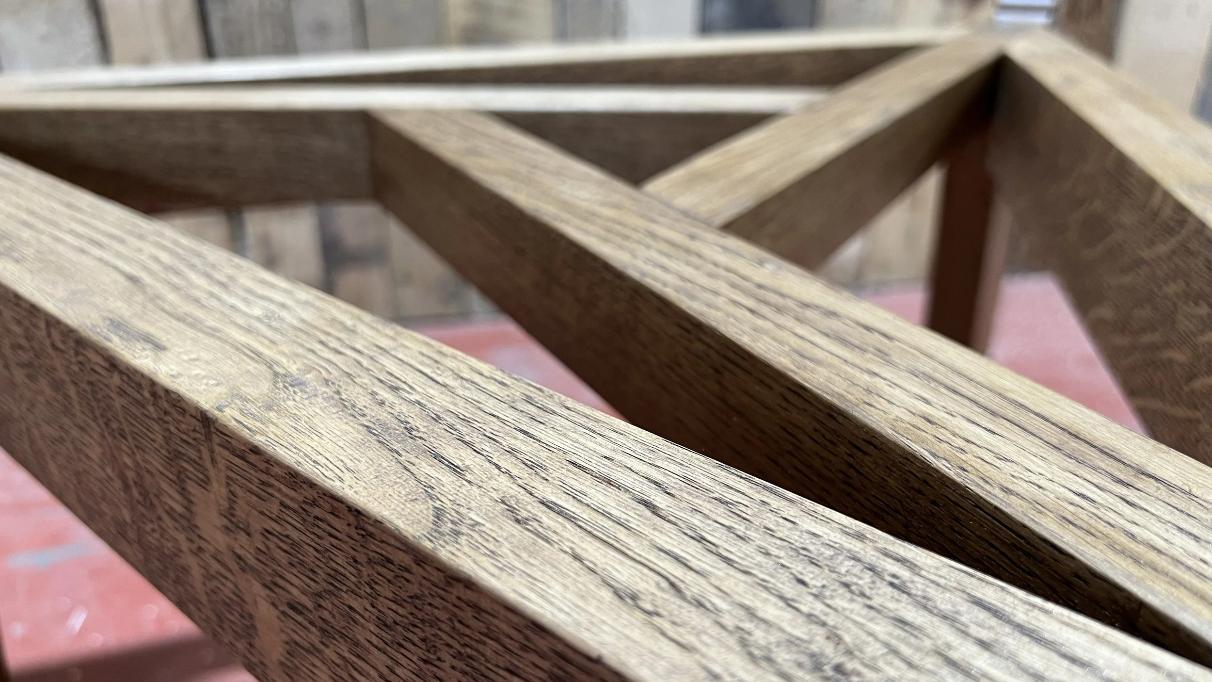 Close-up of wooden furniture frame, showing the textured, natural wood grain, with a brick wall in the background.