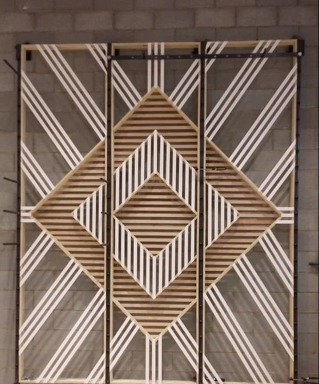 Decorative wall art with geometric patterns of parallel white and brown wooden slats arranged in diamond and triangle shapes against a brick wall background.