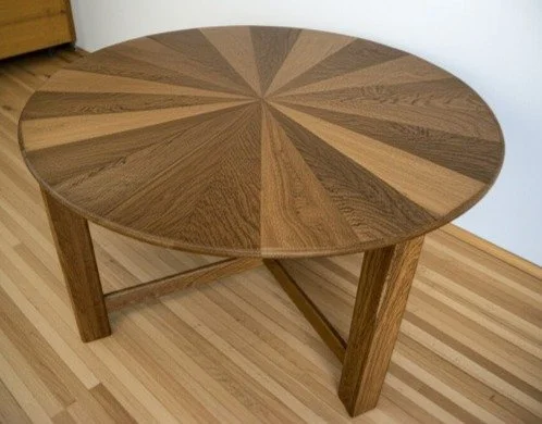 Round wooden table with a starburst pattern inlay on its surface, placed on a hardwood floor.