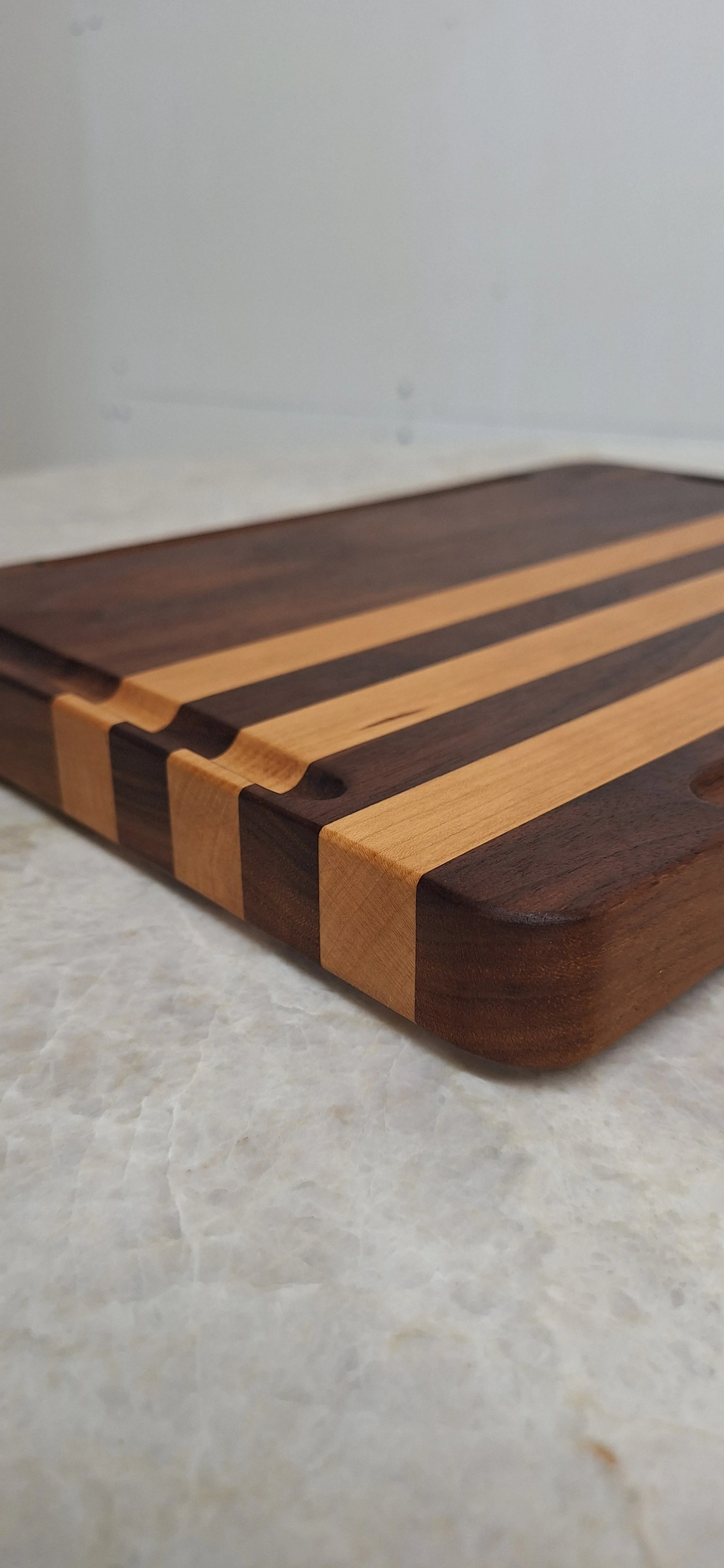 A close-up of a rectangular wooden cutting board with alternating light and dark wood stripes, placed on a light-colored surface.
