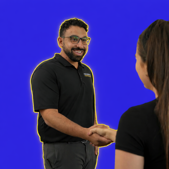 A man with glasses and a beard, wearing a black polo shirt, smiling and shaking hands with a woman in black clothing against a blue background.