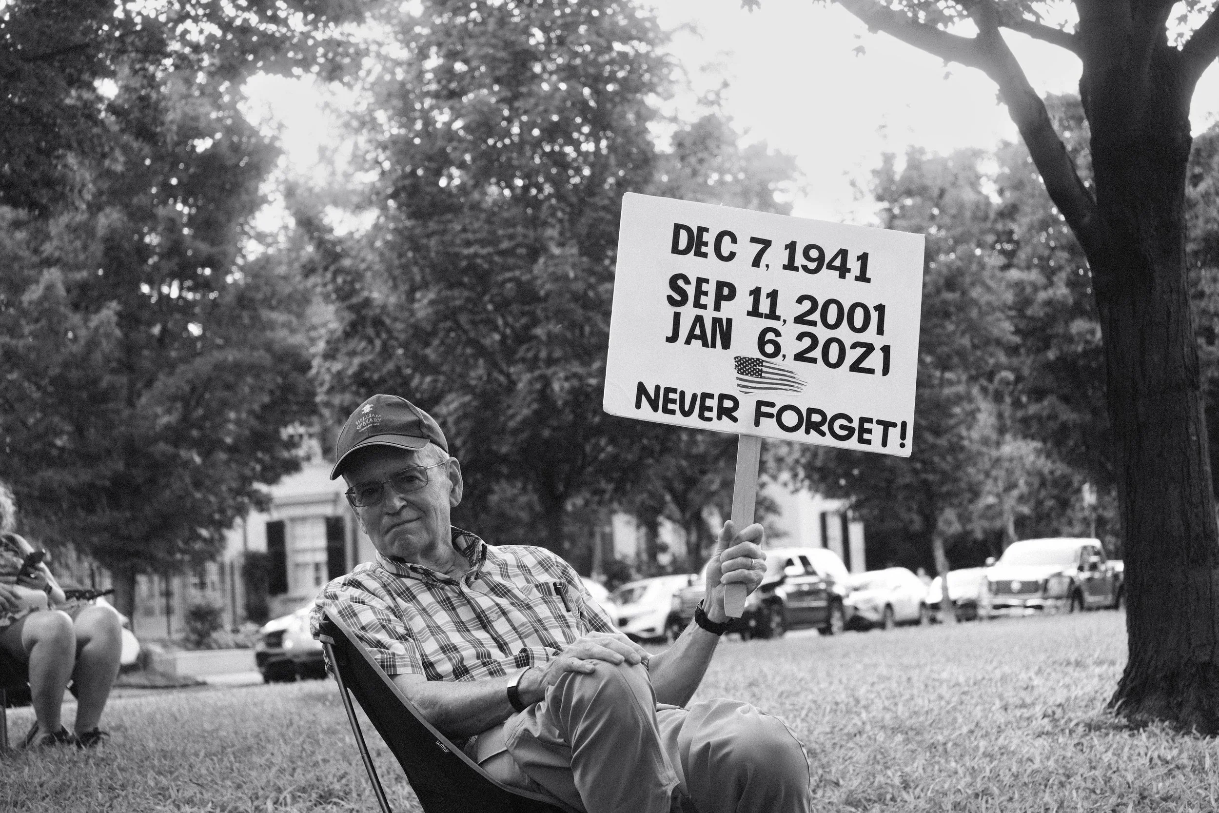 An older man holds a sign advising us to never forget the January 6th coup attempt.