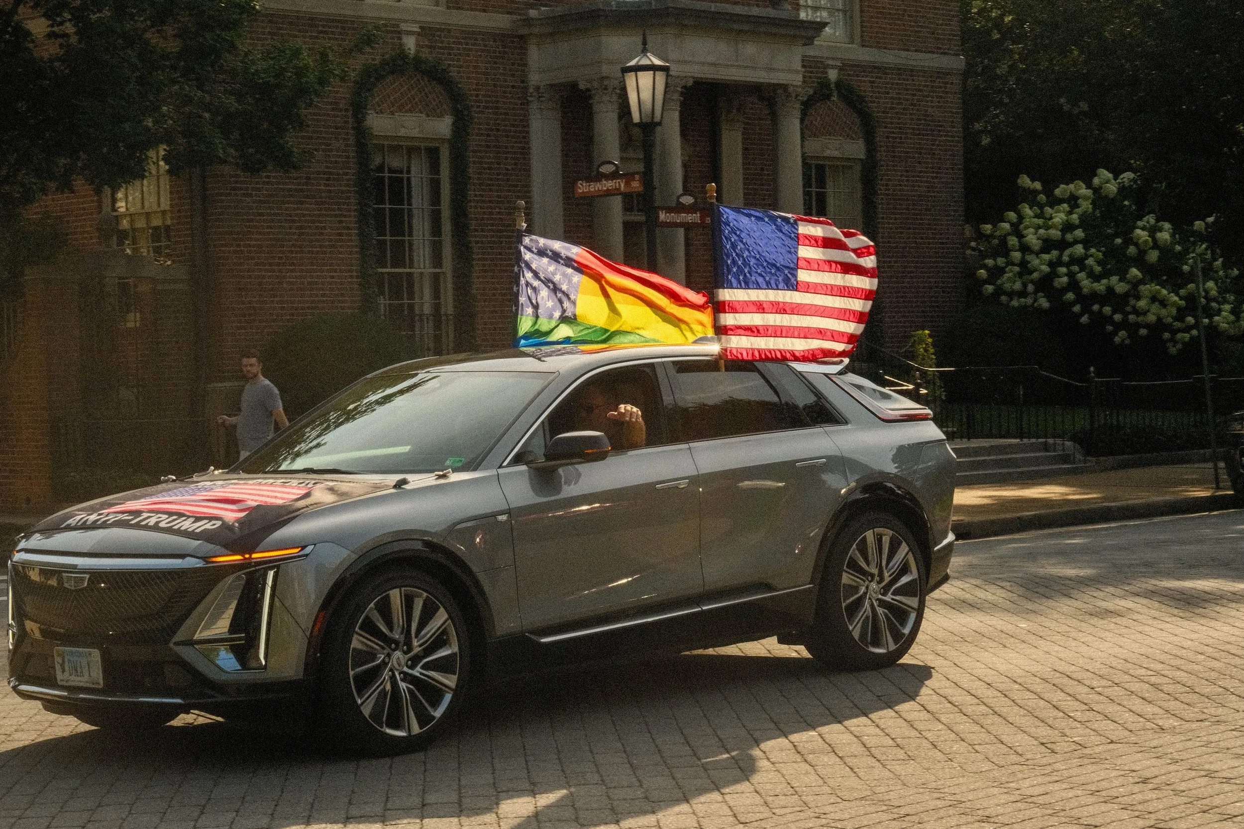 A man driving his car with a pride flag and American flag in support of a protest.