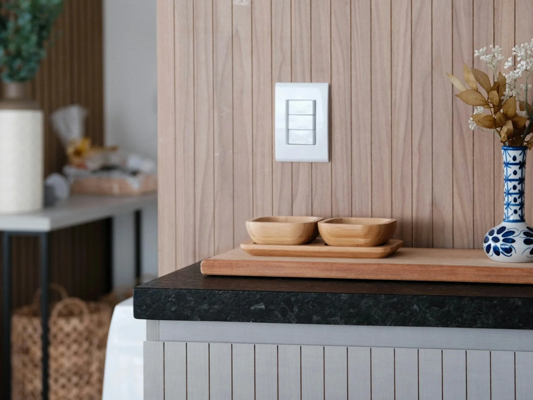 Intérieur avec une table en bois, une vase à fleurs bleue et blanche, deux bols en bois sur un plateau, et un mur en bois clair.