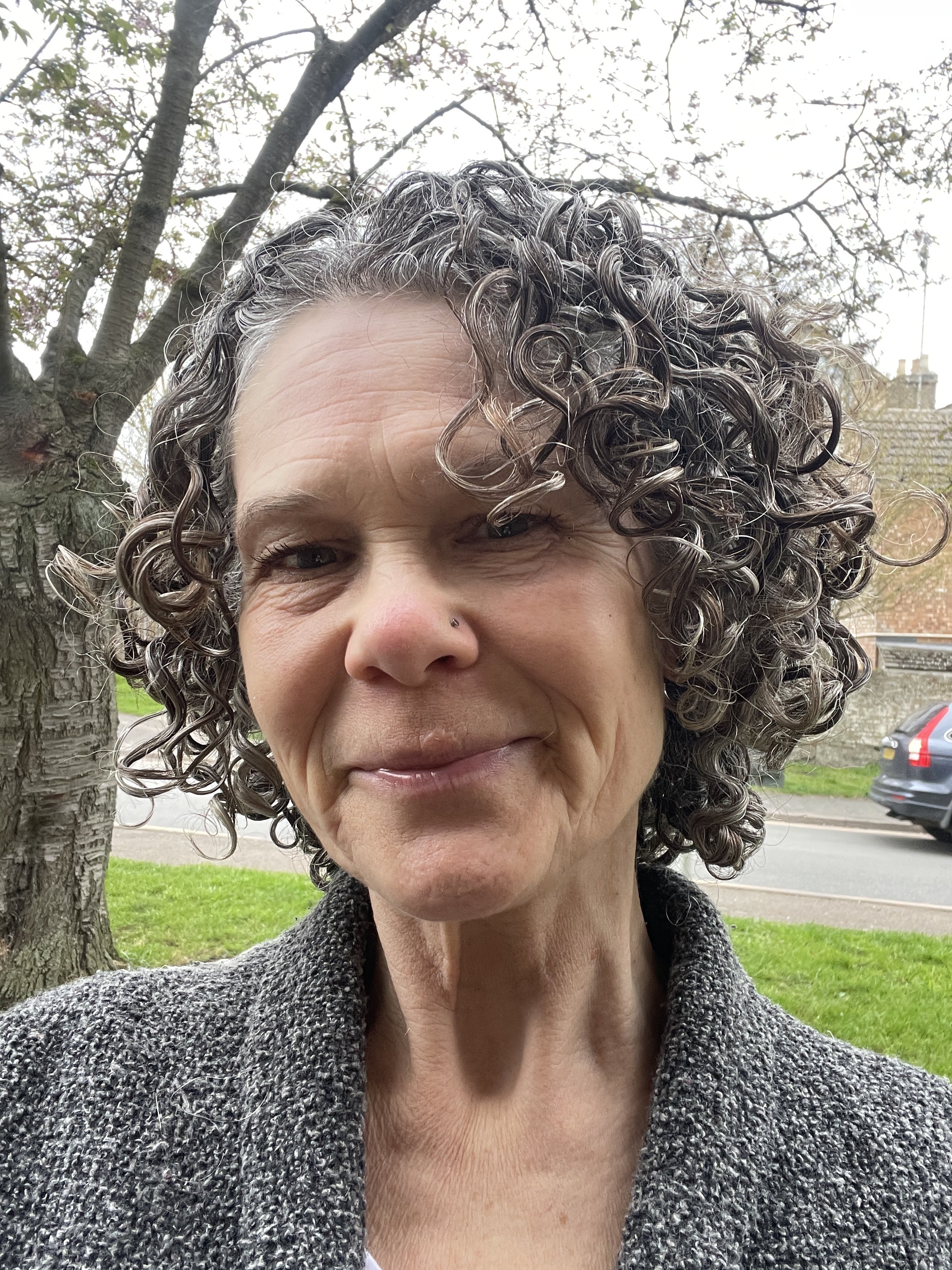 Close-up of Mandy Marty, the Cambridge-based counsellor, with curly hair outdoors with a tree in the background.