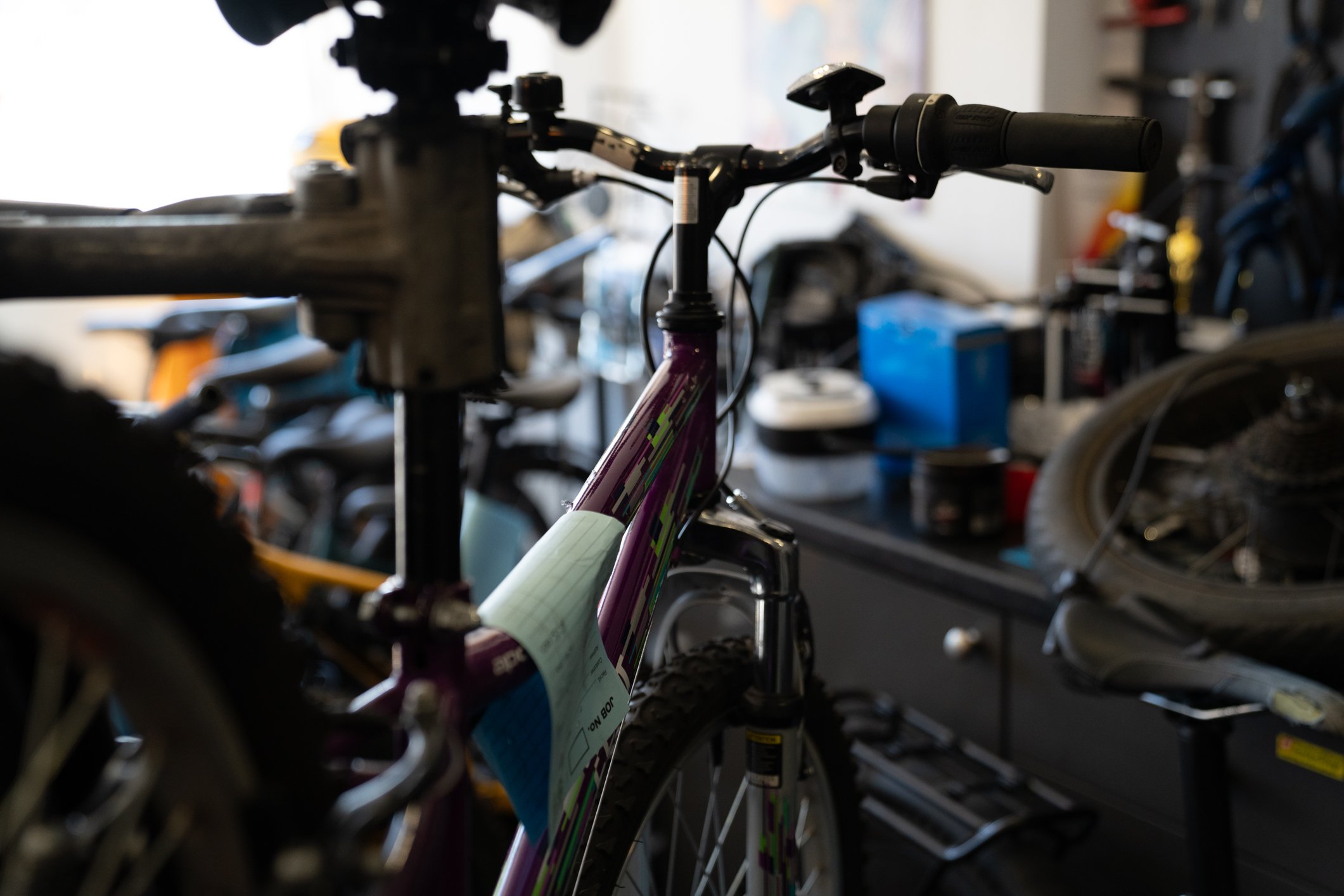 Close-up of a bicycle's handlebars and front frame in a bike shop, with other bicycles and equipment visible in the background.