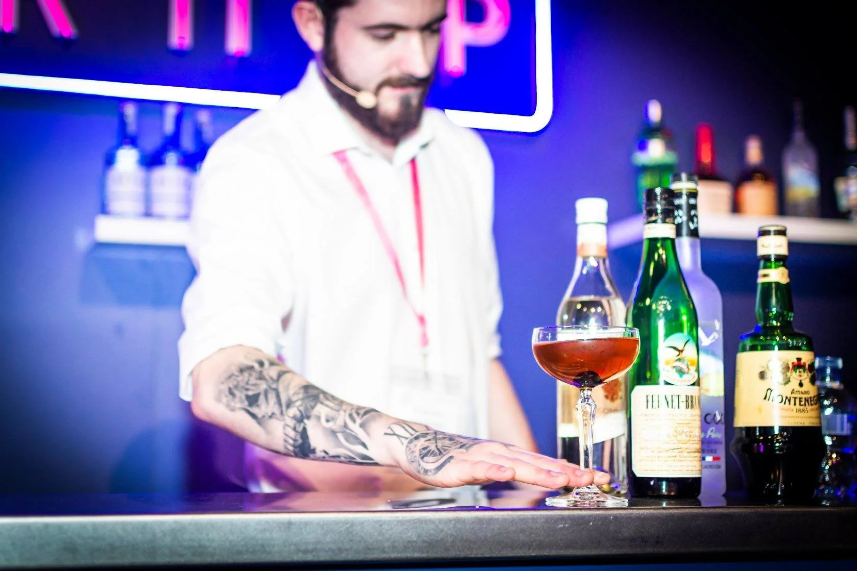 A bartender with a tattooed arm preparing a cocktail at a bar, with various bottles of liquor on the counter taken by south west event photographer