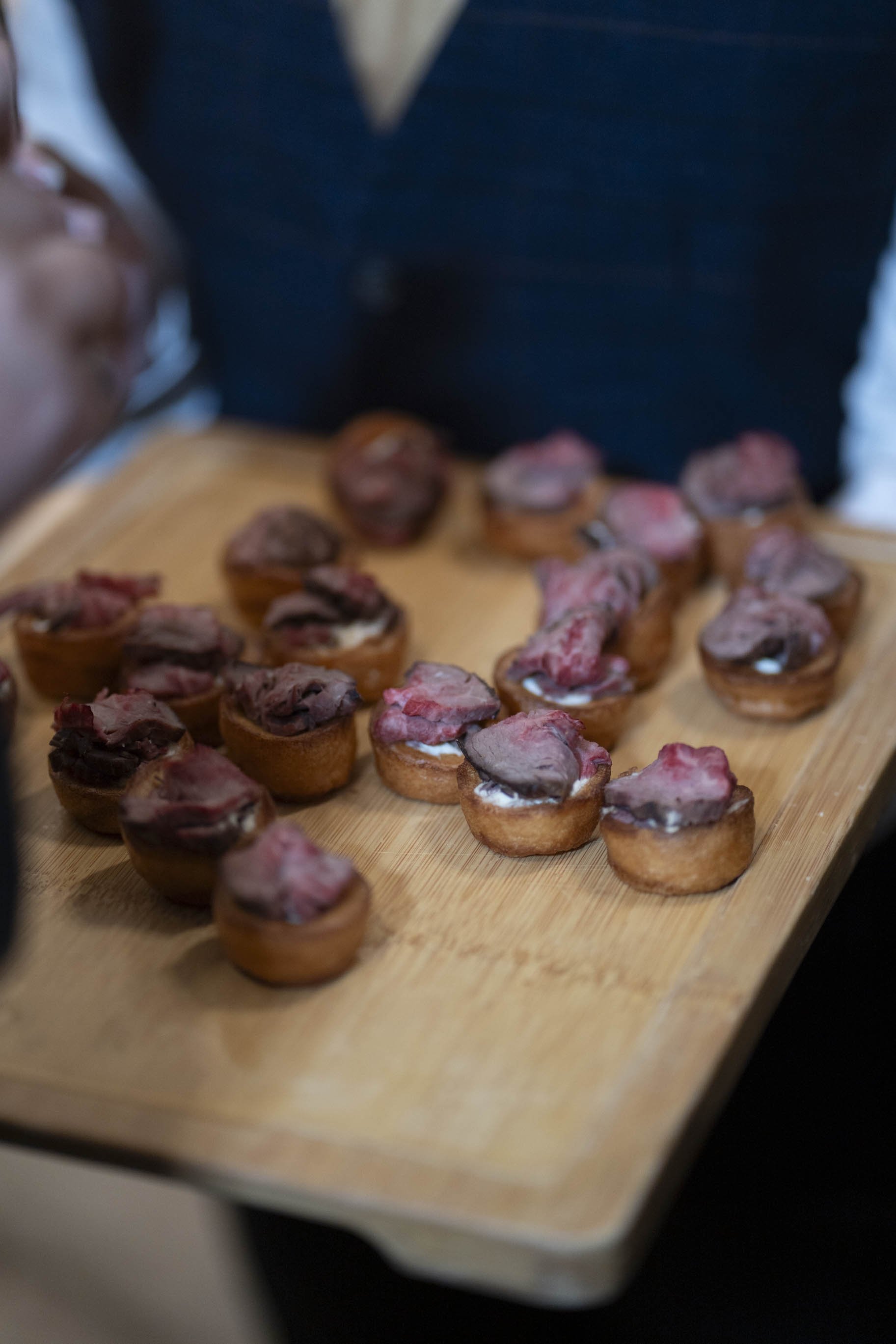 Tray of mini pastry cups topped with various meats and sauces.