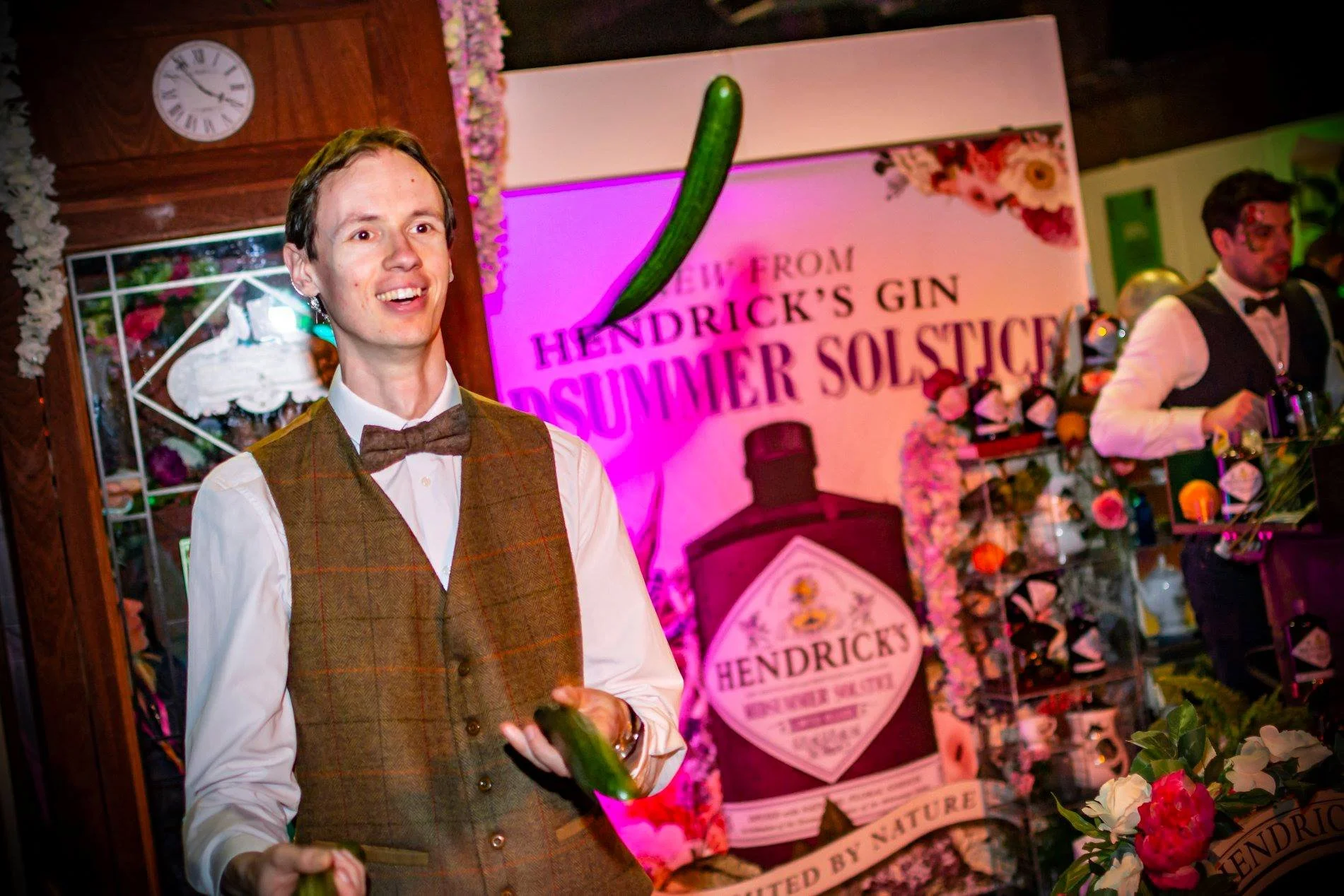 A man dressed in a brown vest and bow tie at an event with a Hendrick's Gin poster and floral decorations in the background taken by south west event photographer