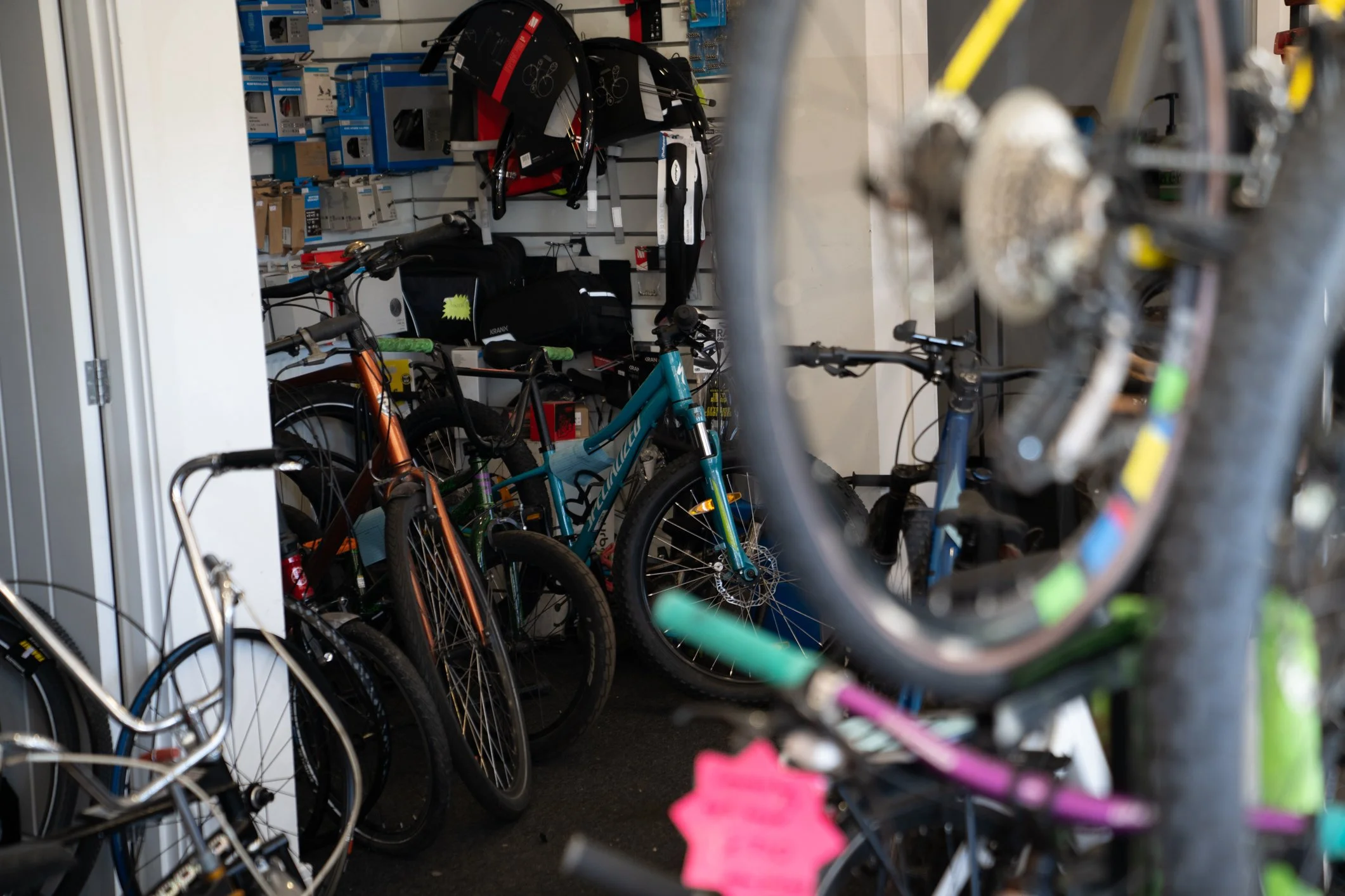 Several bicycles stored in a bike shop, with various bike accessories and parts on the walls.