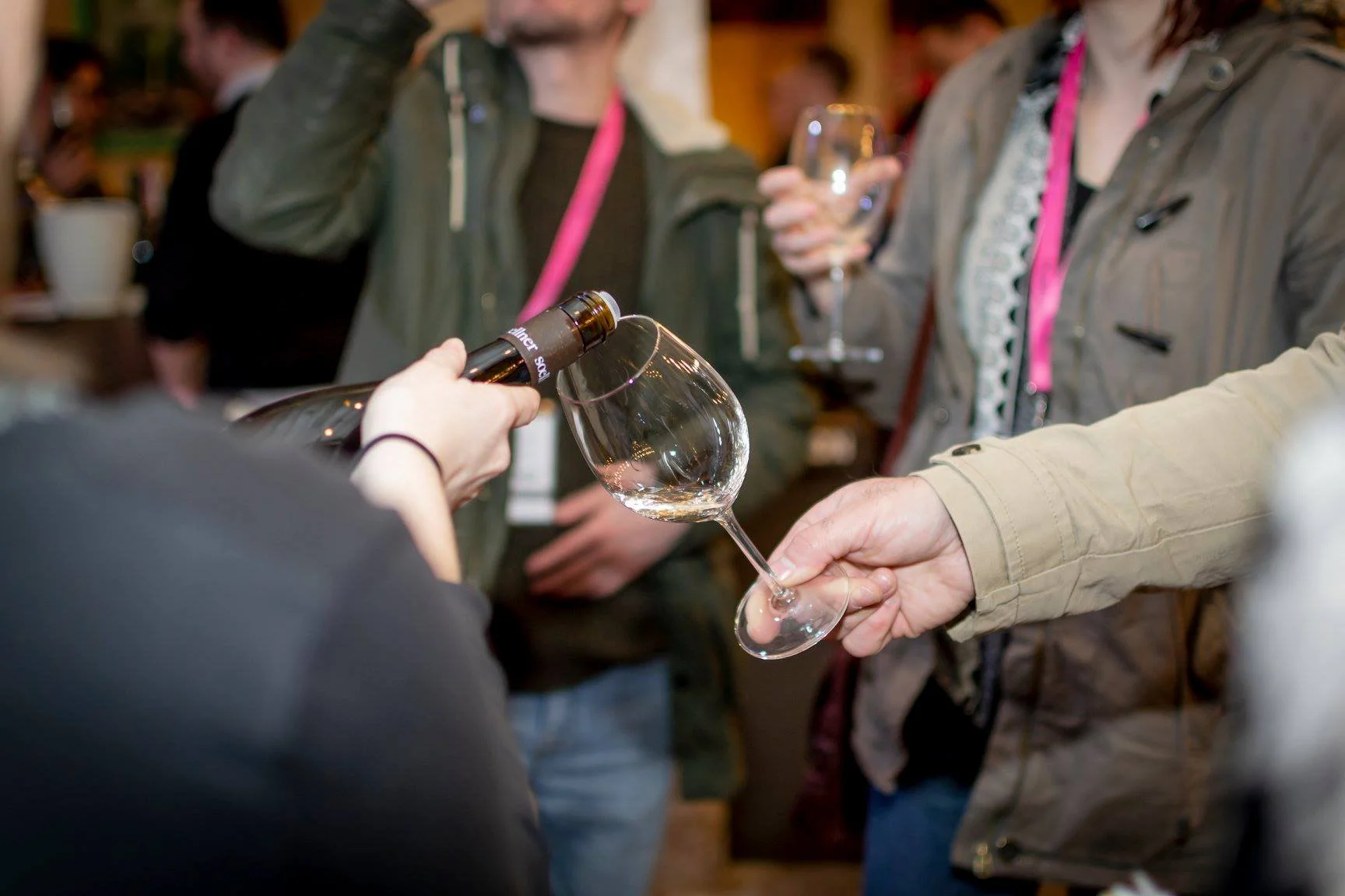 Person pours wine from bottle into glass at a social event with people in the background holding glasses taken by Bristol event photographer