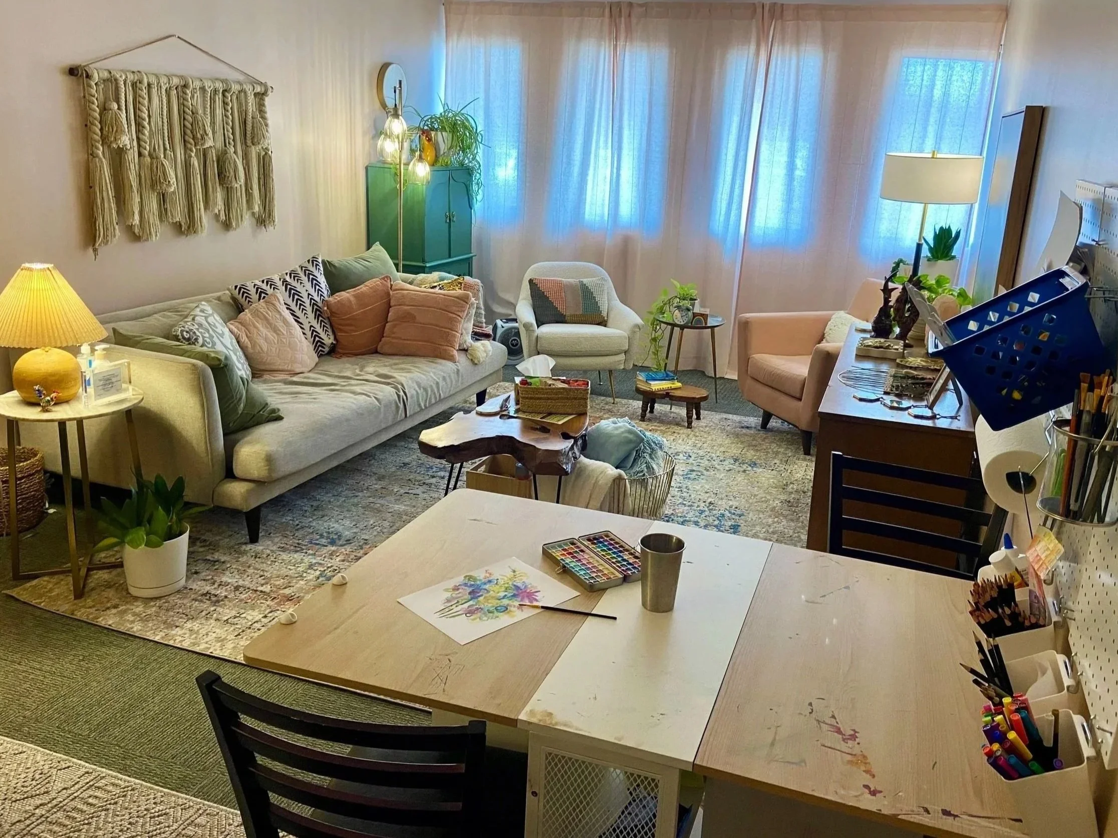 Cozy counseling office with pastel-colored furniture, plants, and an art therapy table.