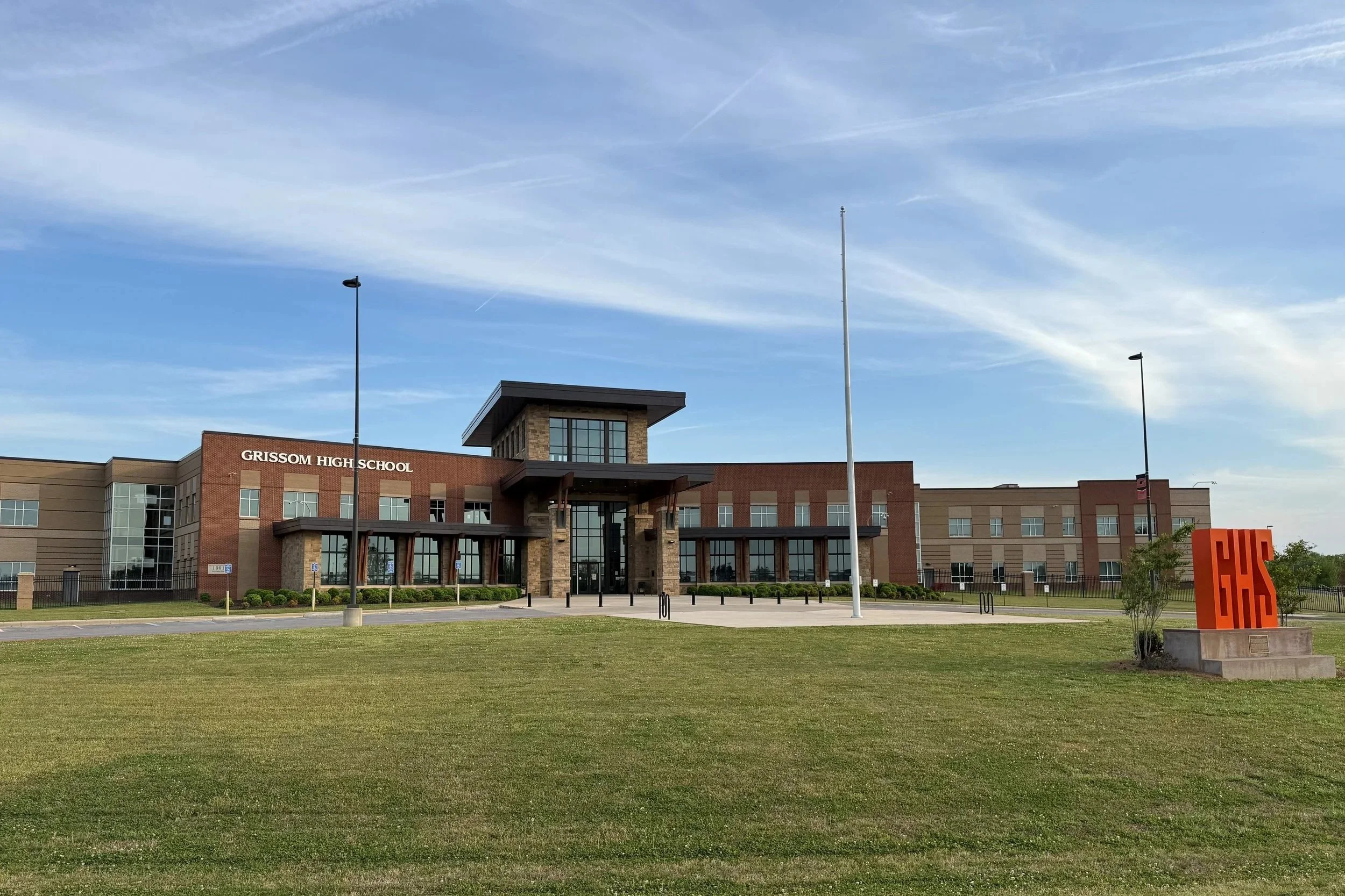 Exterior view of Grissom High School building with a lawn in foreground, flagpole, and blue sky.