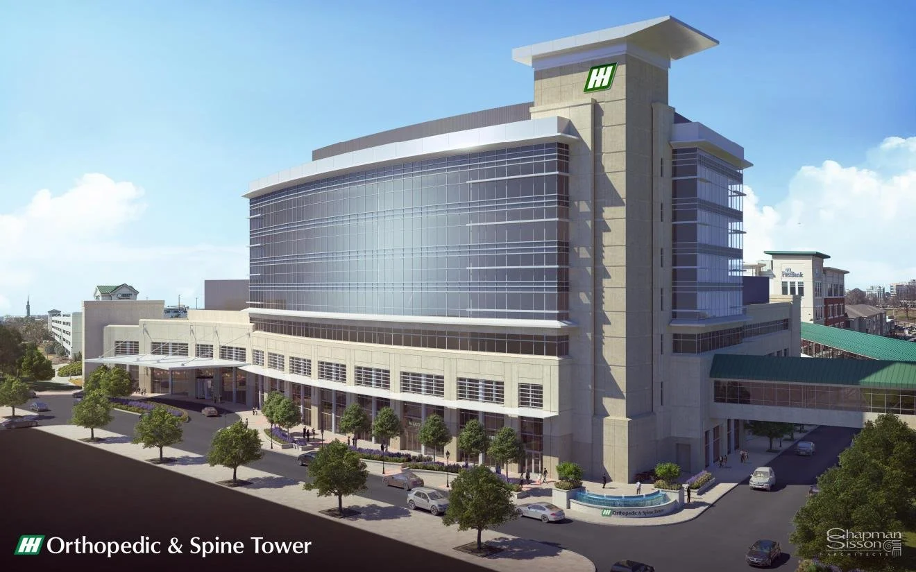 West bed tower - Huntsville Hospital. A modern hospital building rendering with a glass facade and multiple floors, named Holtic and Spine Tower, surrounded by a parking lot with cars and trees, under a partly cloudy sky.