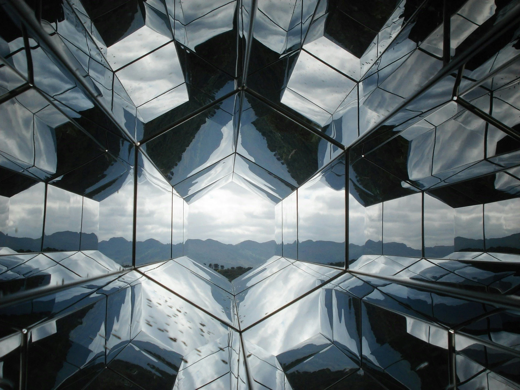 Reflection of cloudy sky and mountains on a mirrored geometric building facade.