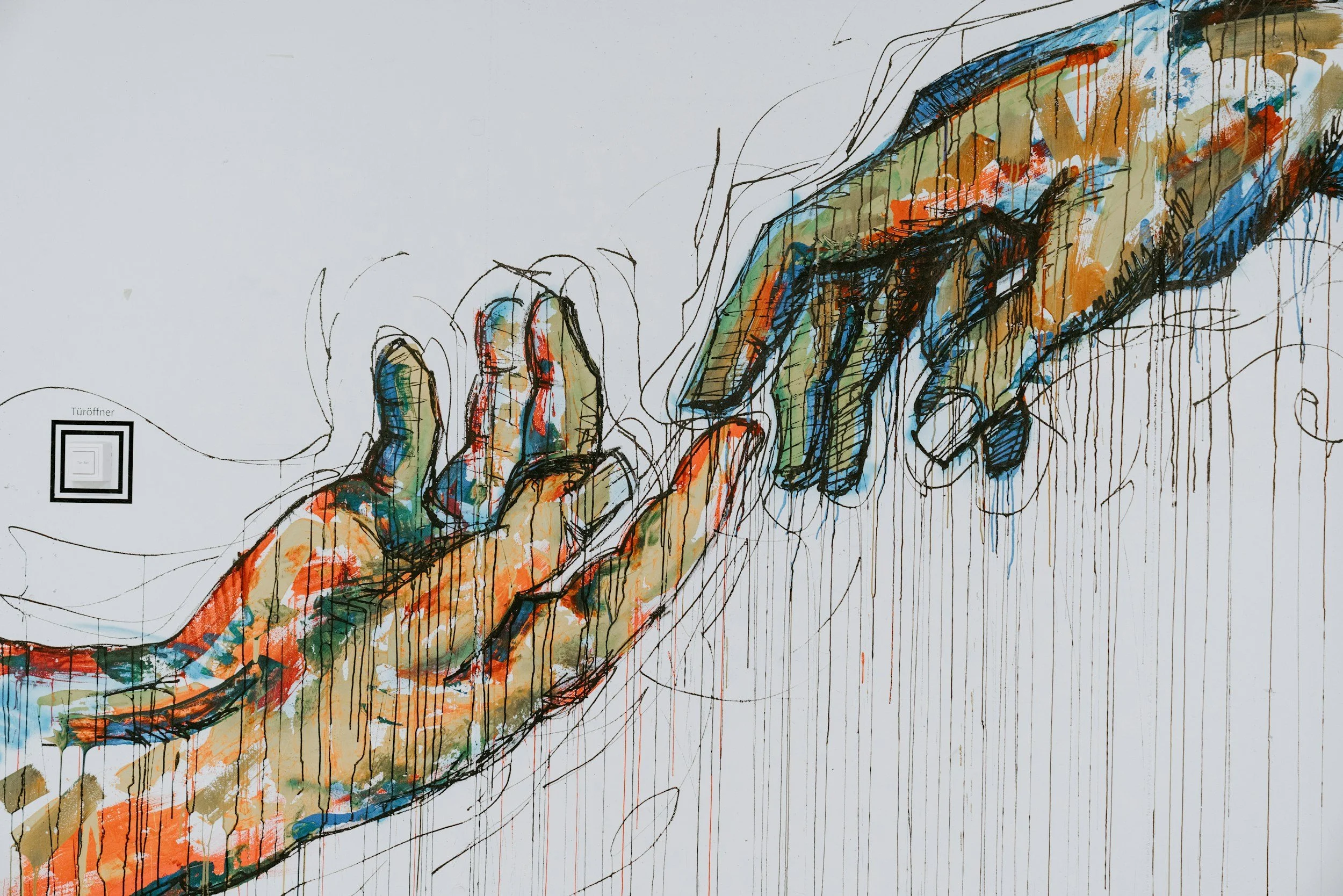 Colorful artwork of two hands reaching toward each other, with visible sketch lines and paint drips, on a white background.