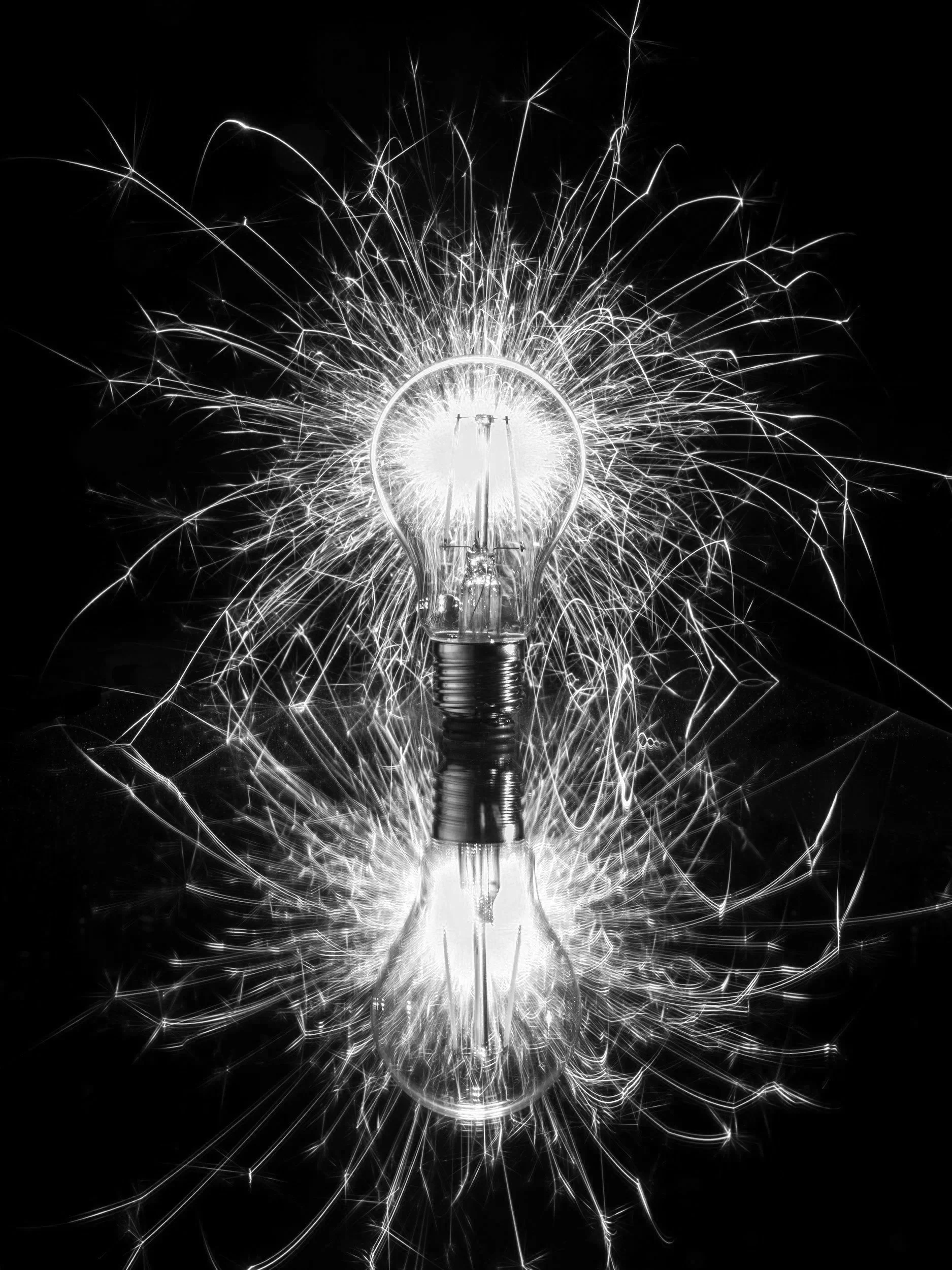 A light bulb with sparks flying around and reflecting on a black surface.