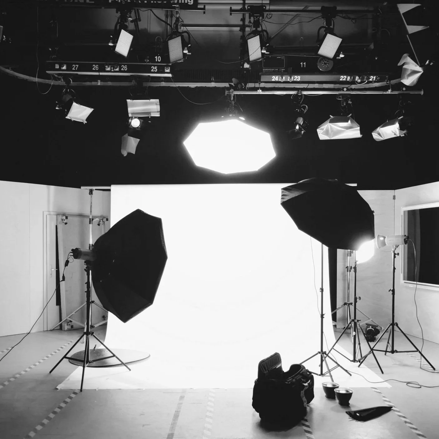 A professional photography or filming studio setup with lighting equipment, umbrellas, softboxes, and a white backdrop.
