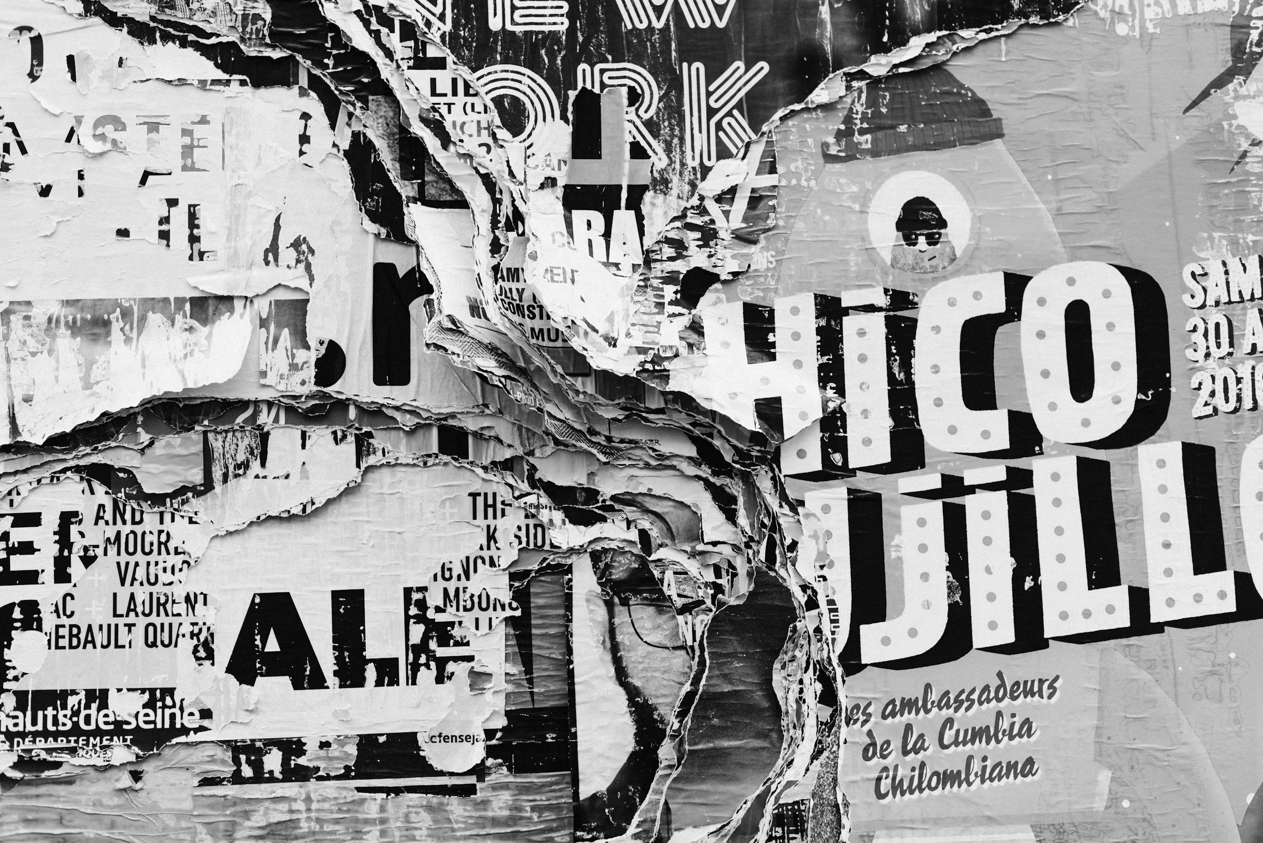 A black and white photo of torn posters layered over each other on a wall, with some text and graphics visible through the torn paper.