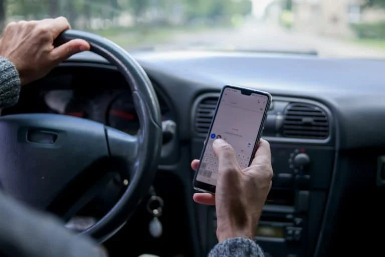 Person holding a smartphone while driving a car on a rural road