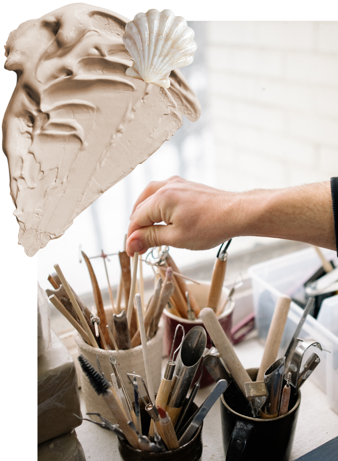 Close-up of a sculptor's hand reaching into a container of sculpting tools, with a large seashell and a clay or plaster sculpture in the background.