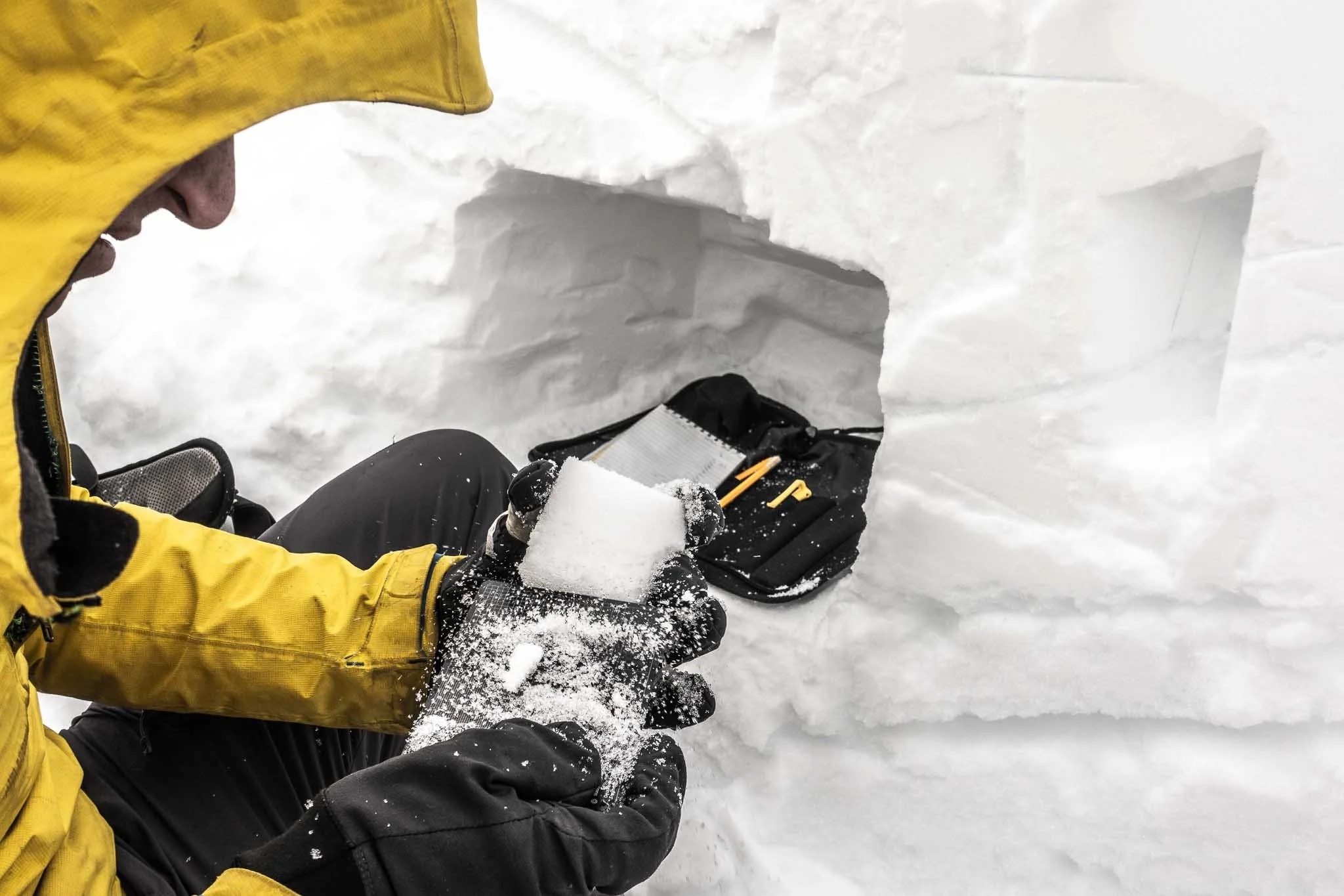 Person i gul jakke lager isblokker i et snødekt område, med en ishule i bakgrunnen.