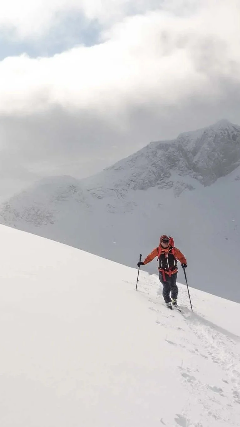 Person som går på snø med fjell i bakgrunnen og skyet vær