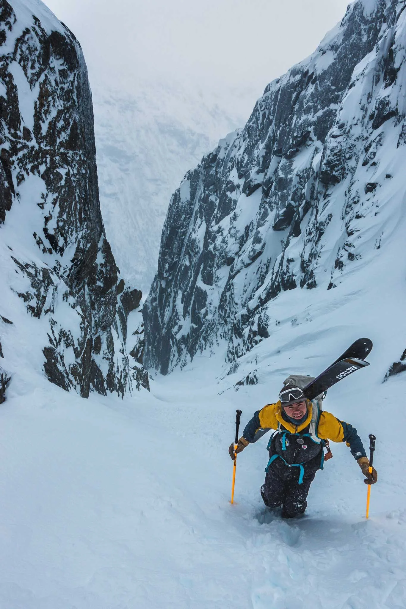 En person i fjellklatrerutstyr som klatrer opp i en snødekt fjellkløft, omgitt av høye snødekte fjellvegger.
