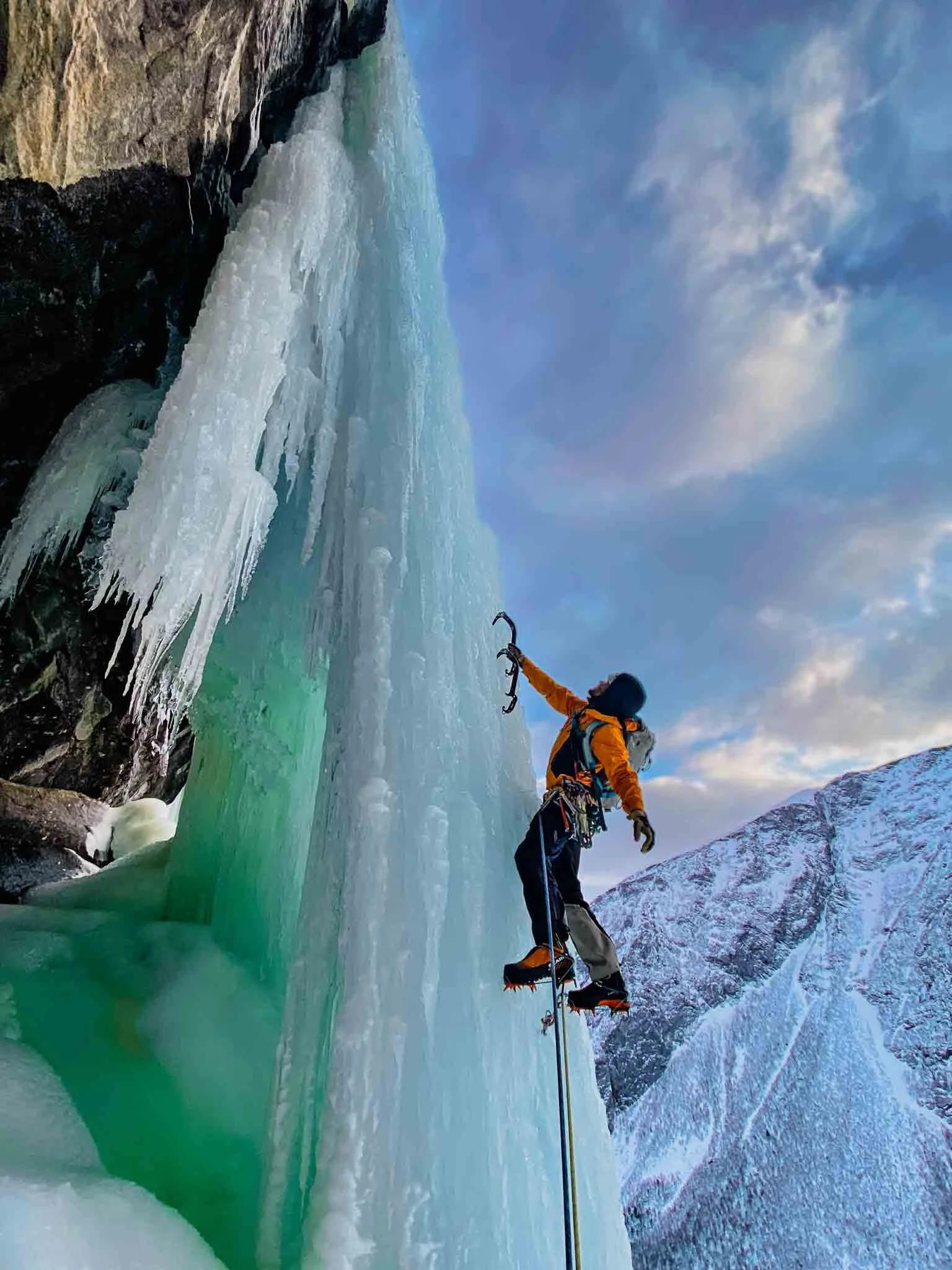 Fjellklatrer med isøks nær en stor, frossen foss i snødekte fjell.