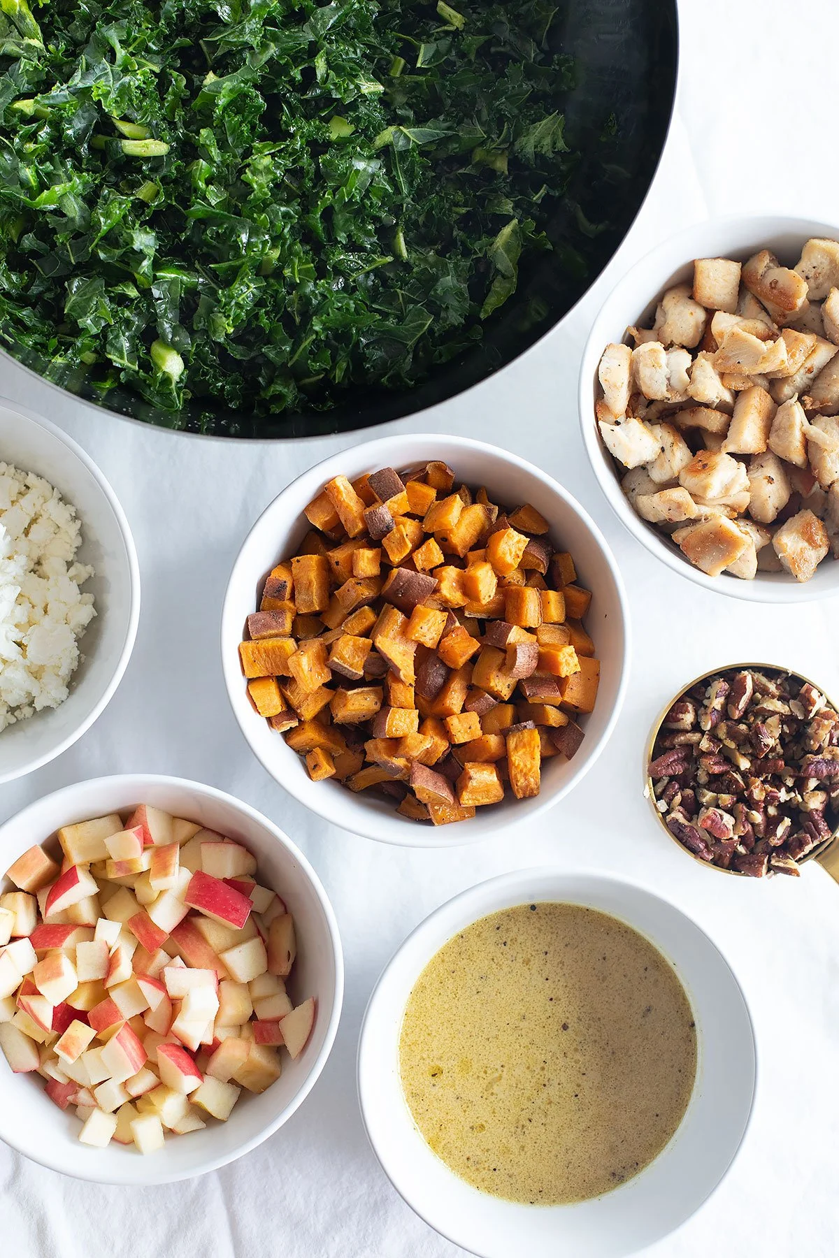 Ingredients for fall kale and apple salad including kale, apples, roasted sweet potatoes, chicken, pecans, feta, and maple mustard dressing.