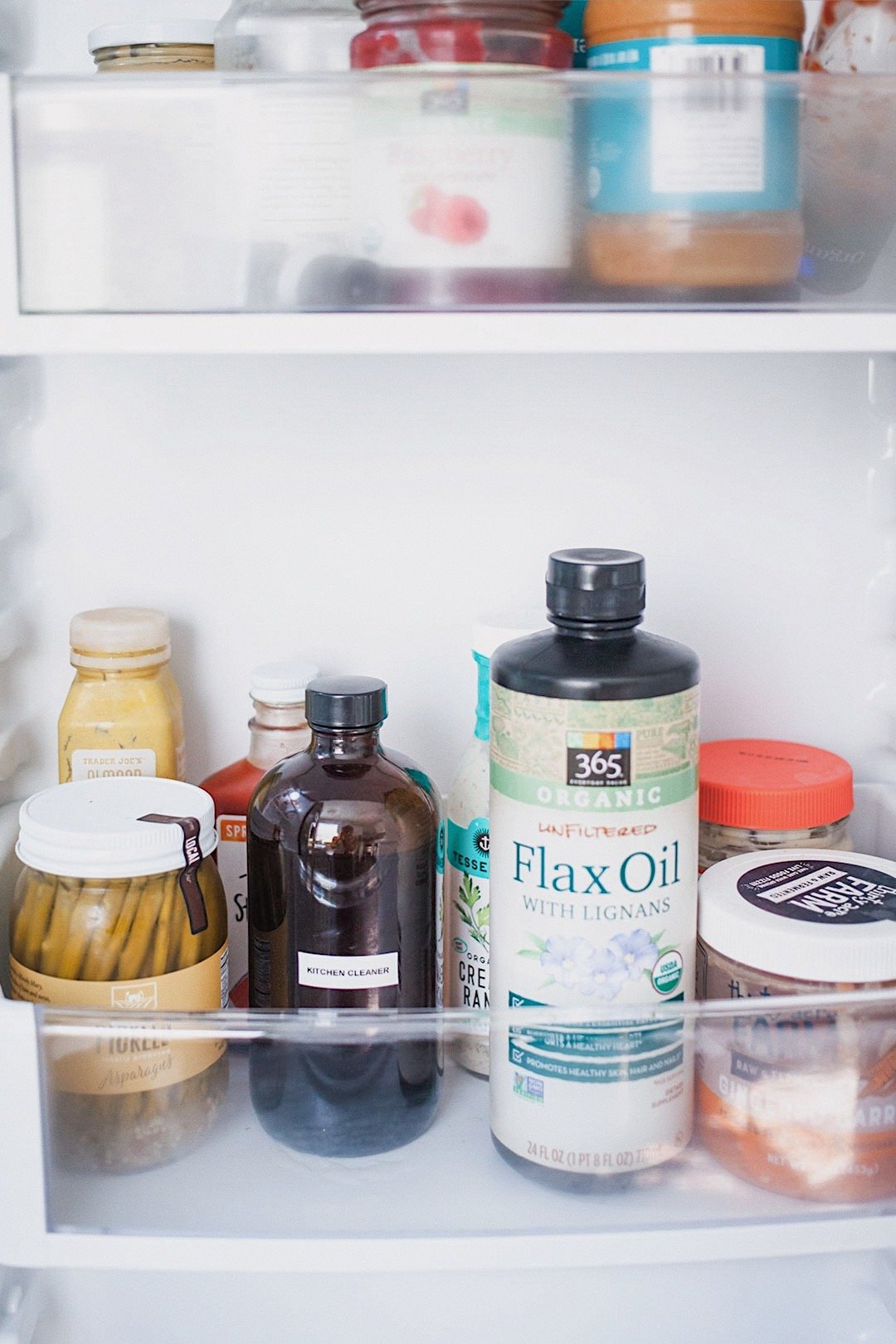 Amber glass bottle of natural kitchen cleaner stored in a refrigerator door next to condiments and flax oil.