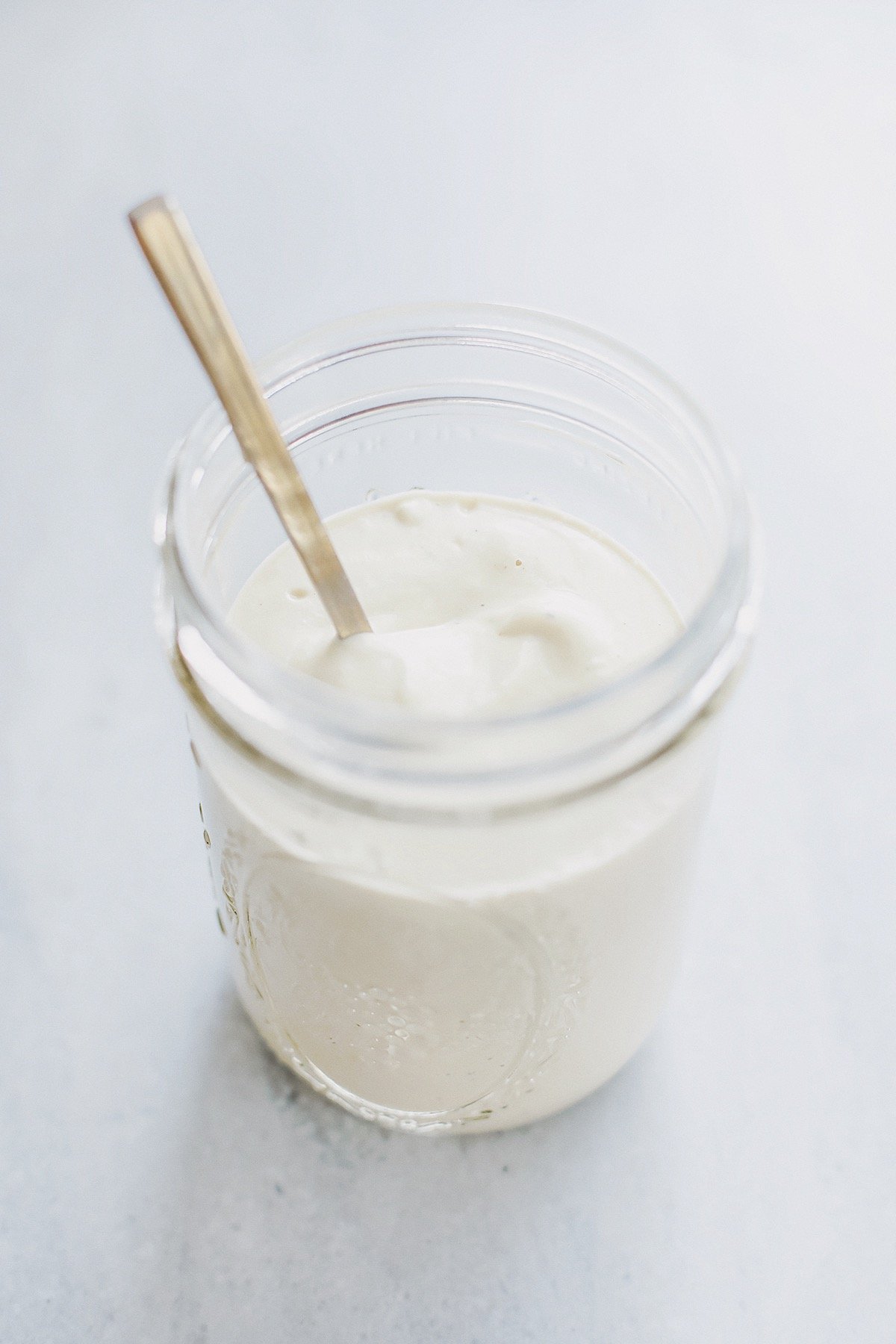 Creamy dairy-free cashew alfredo sauce in a glass jar with spoon on neutral background.