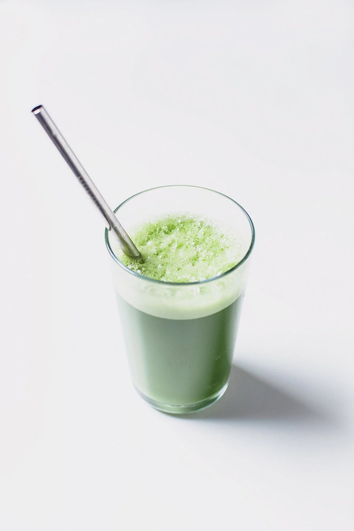 Green juice in a clear glass with straw on white background.