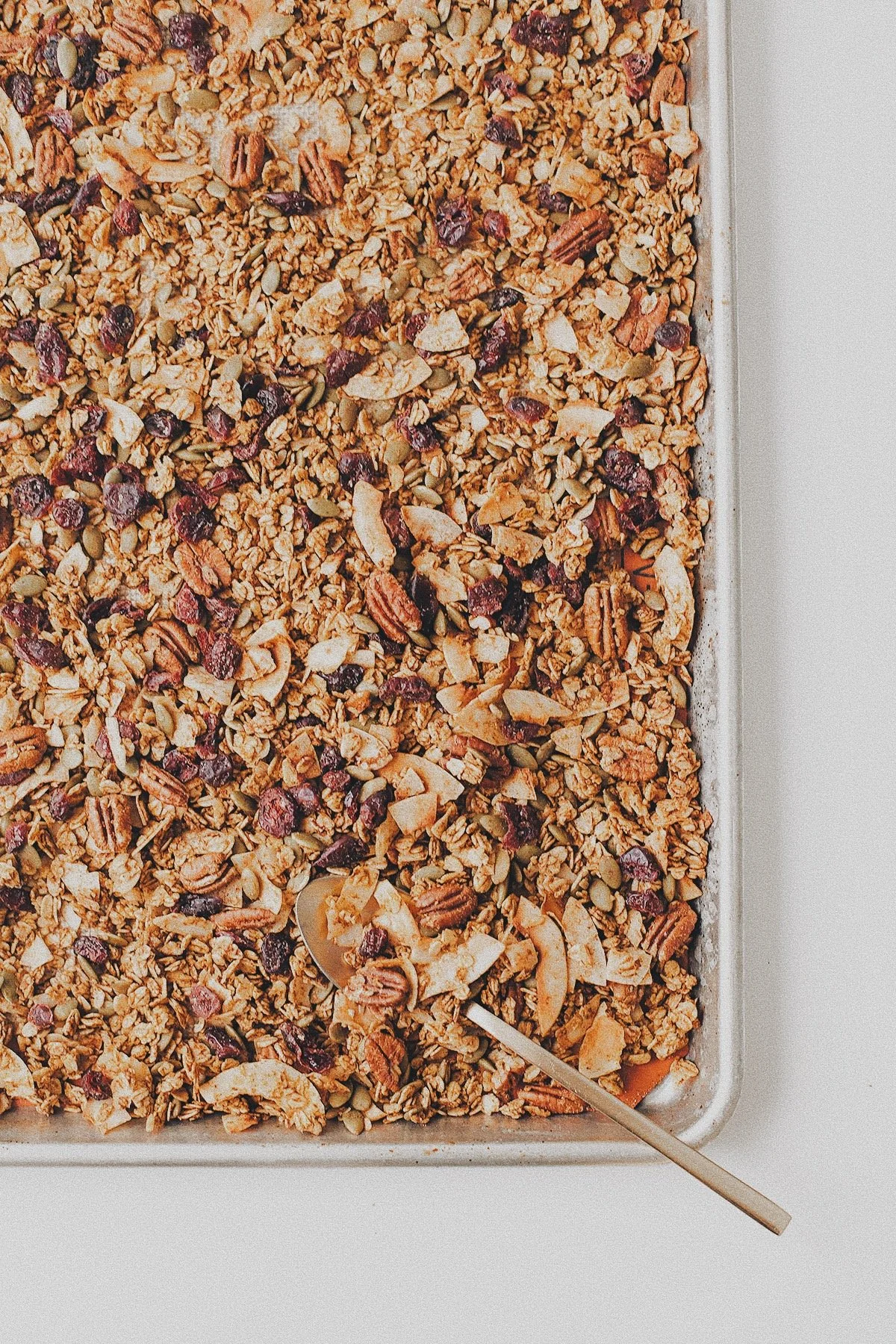 Low-sugar pumpkin granola with oats, pecans, pumpkin seeds, coconut, and dried cranberries on a baking sheet.