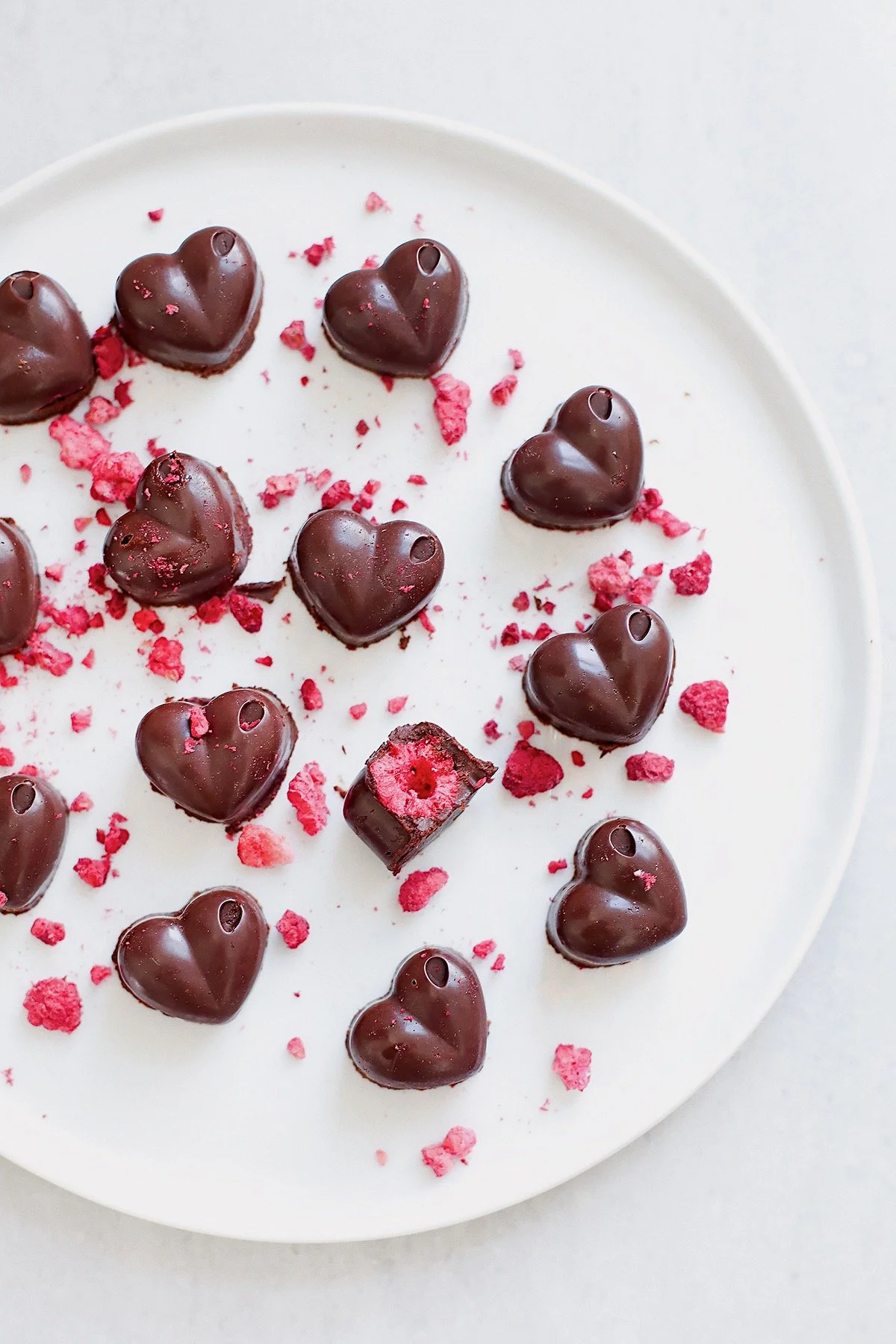Easy homemade raspberry chocolates on white plate with crushed raspberries on top.